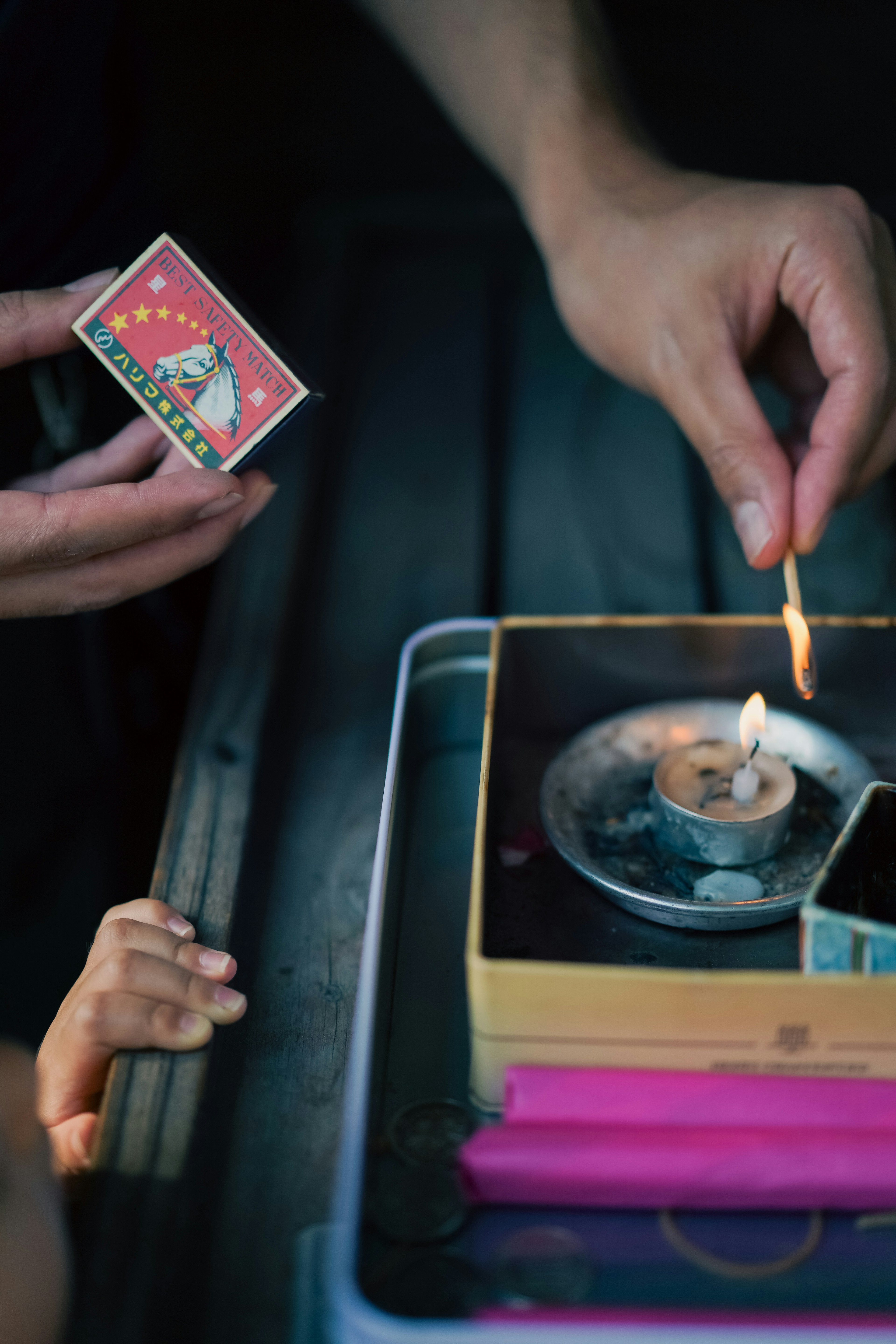 An adult hand holding a match and lighting a candle with a child's hand visible