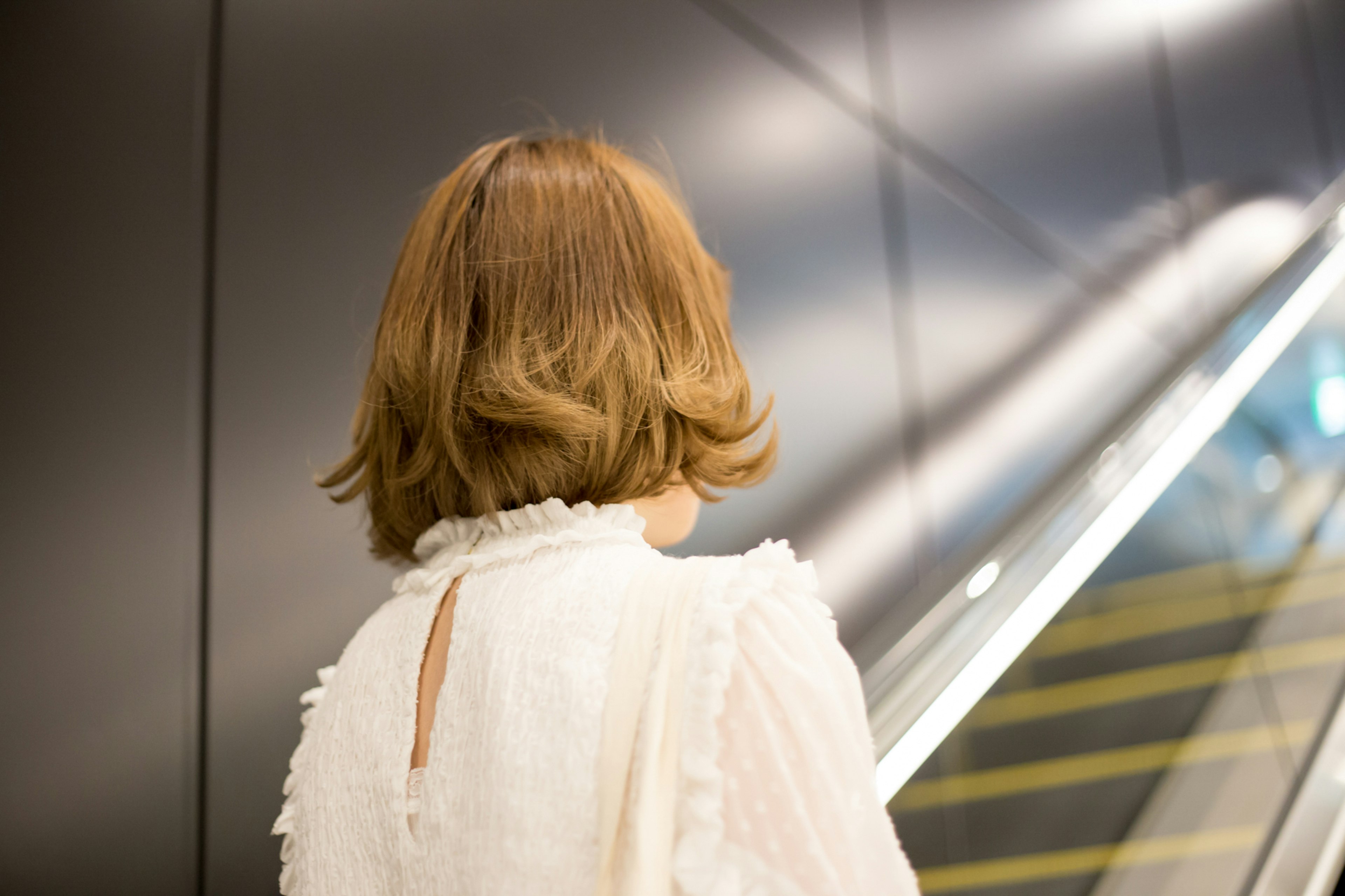 A woman standing with her back facing the camera featuring a bob hairstyle and a white outfit