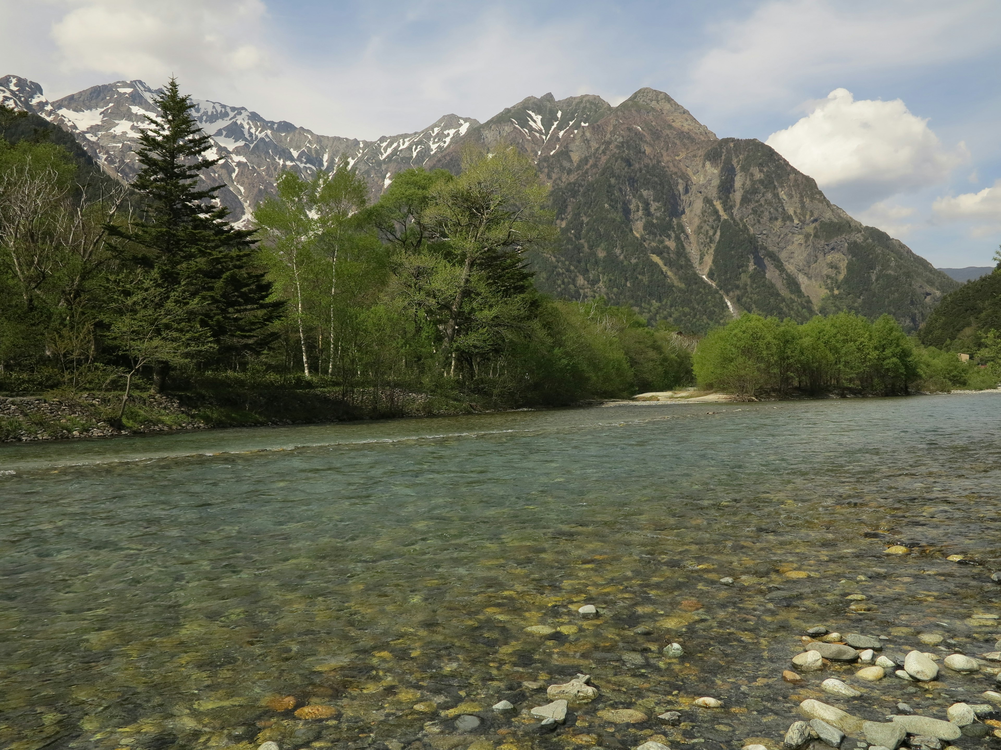 Pemandangan sungai jernih dikelilingi pegunungan dan pohon hijau