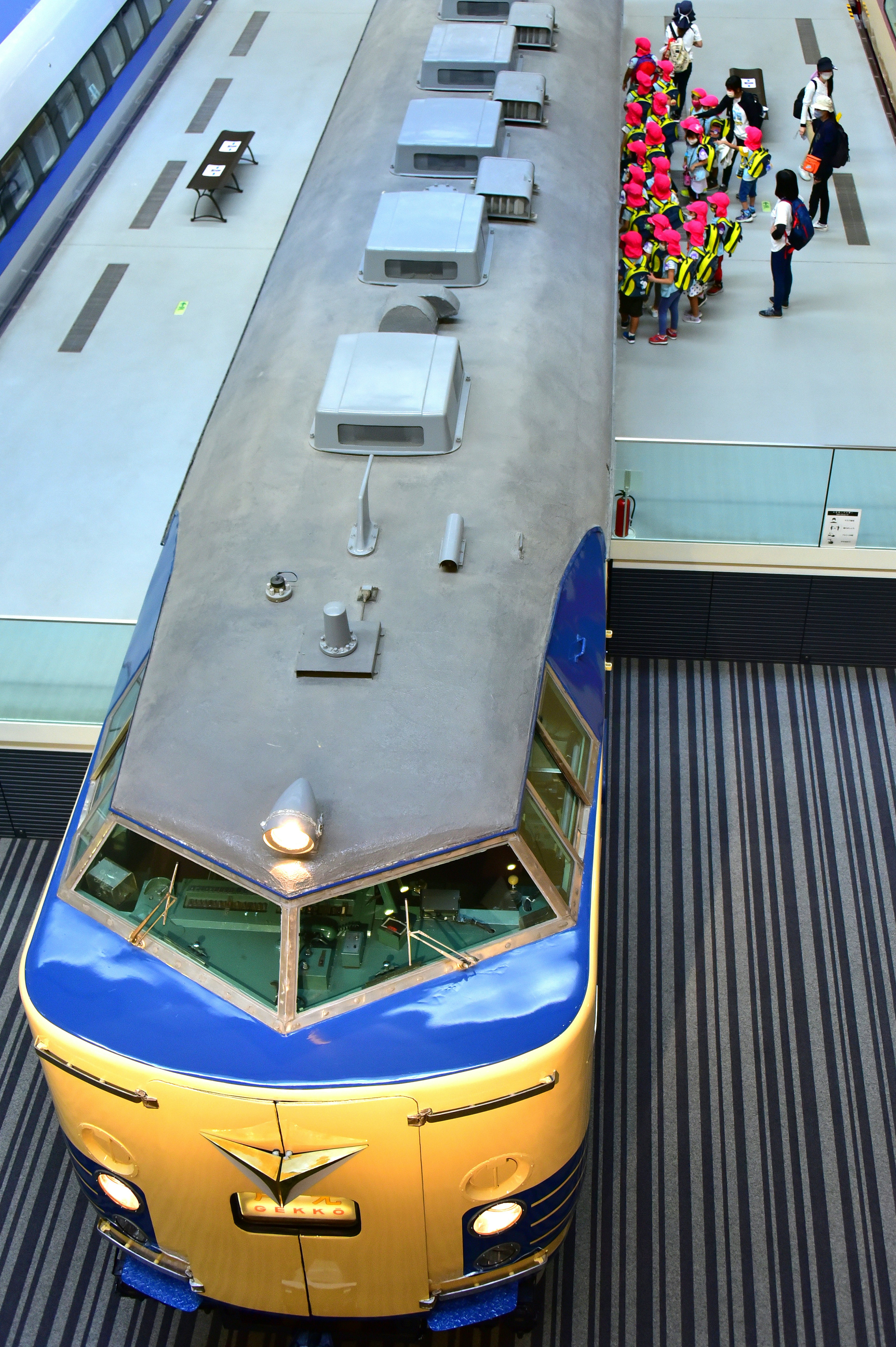 A blue and yellow train at a station viewed from above people holding bouquets nearby