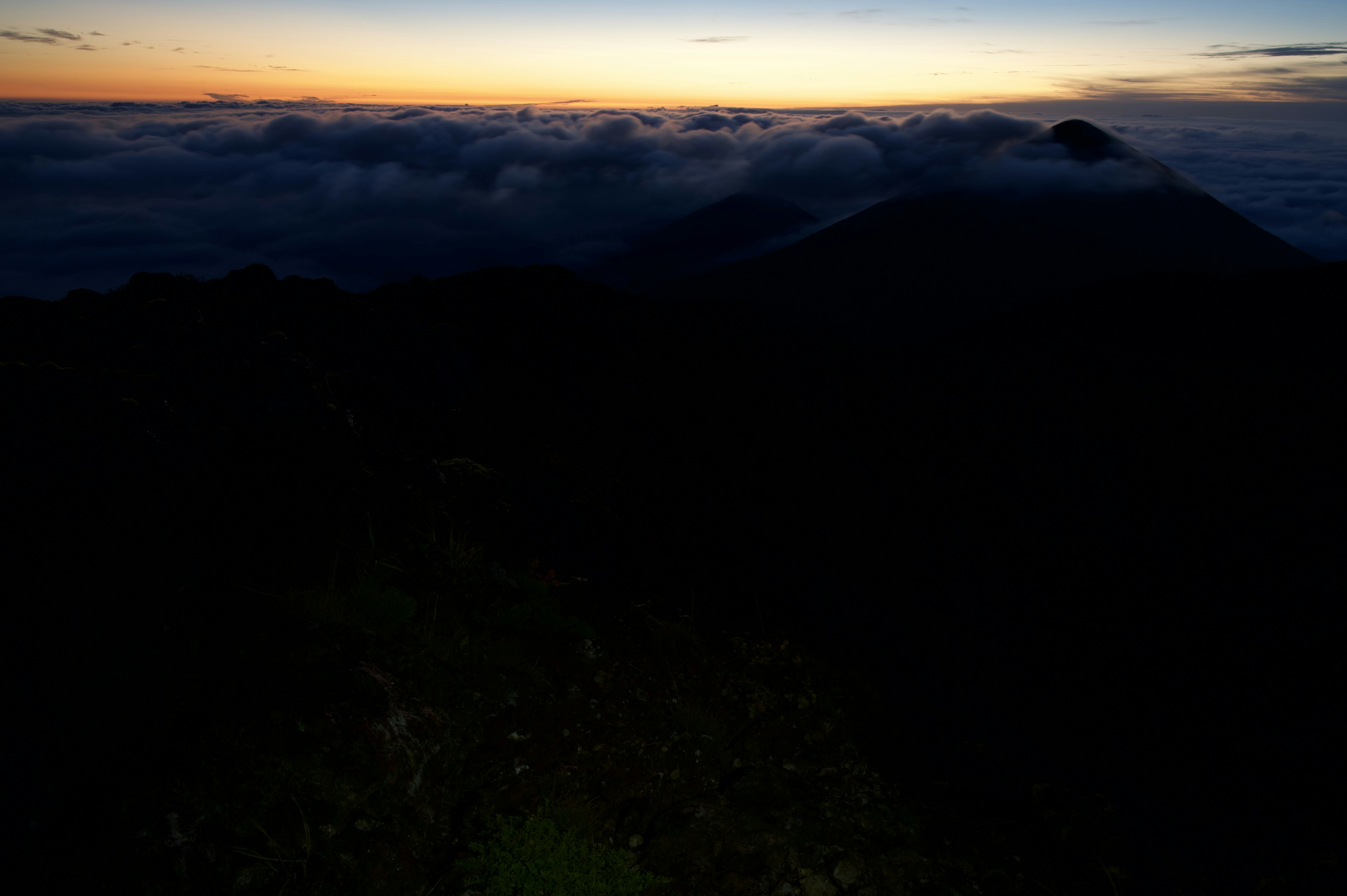 Silhouette di una montagna contro un mare di nuvole al tramonto