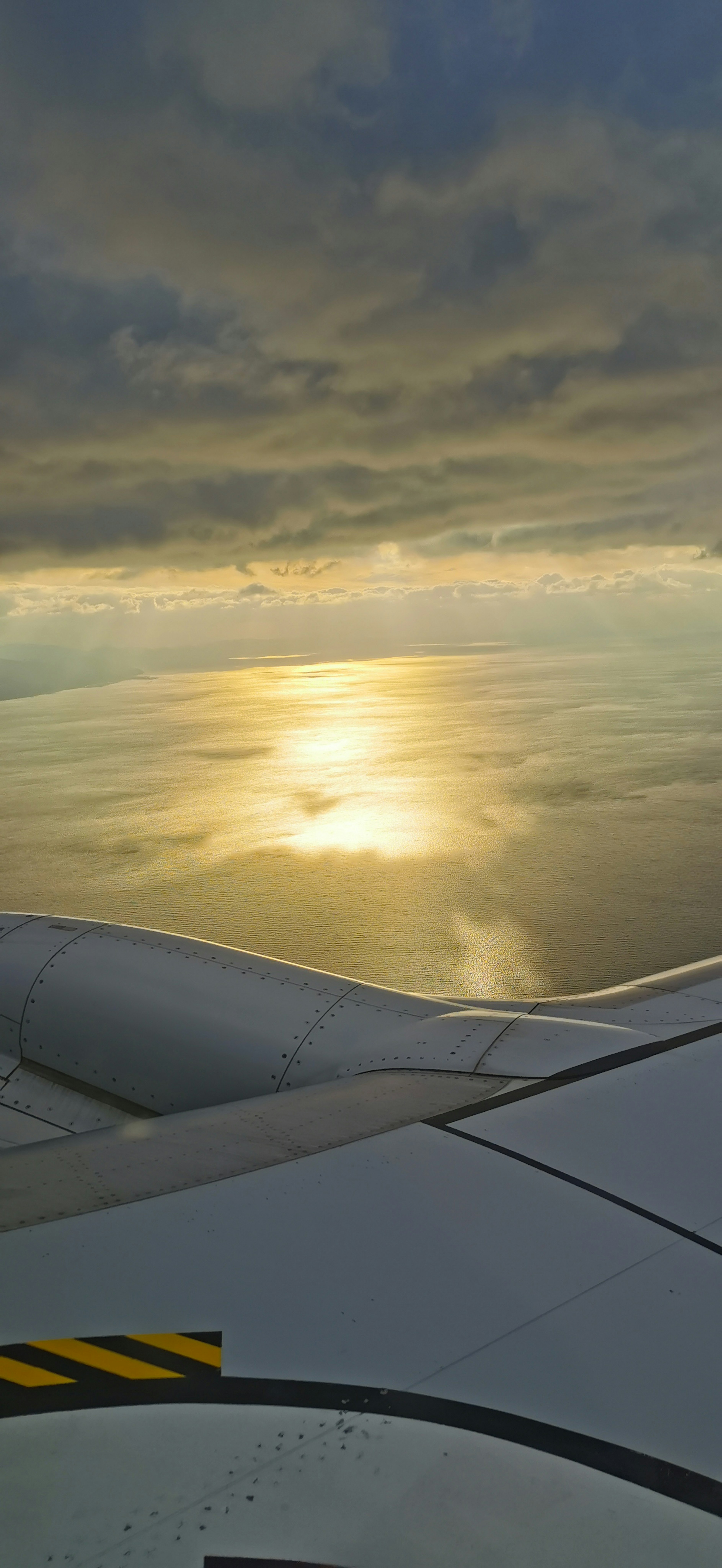 Photo d'une aile d'avion avec des nuages et le reflet de l'océan