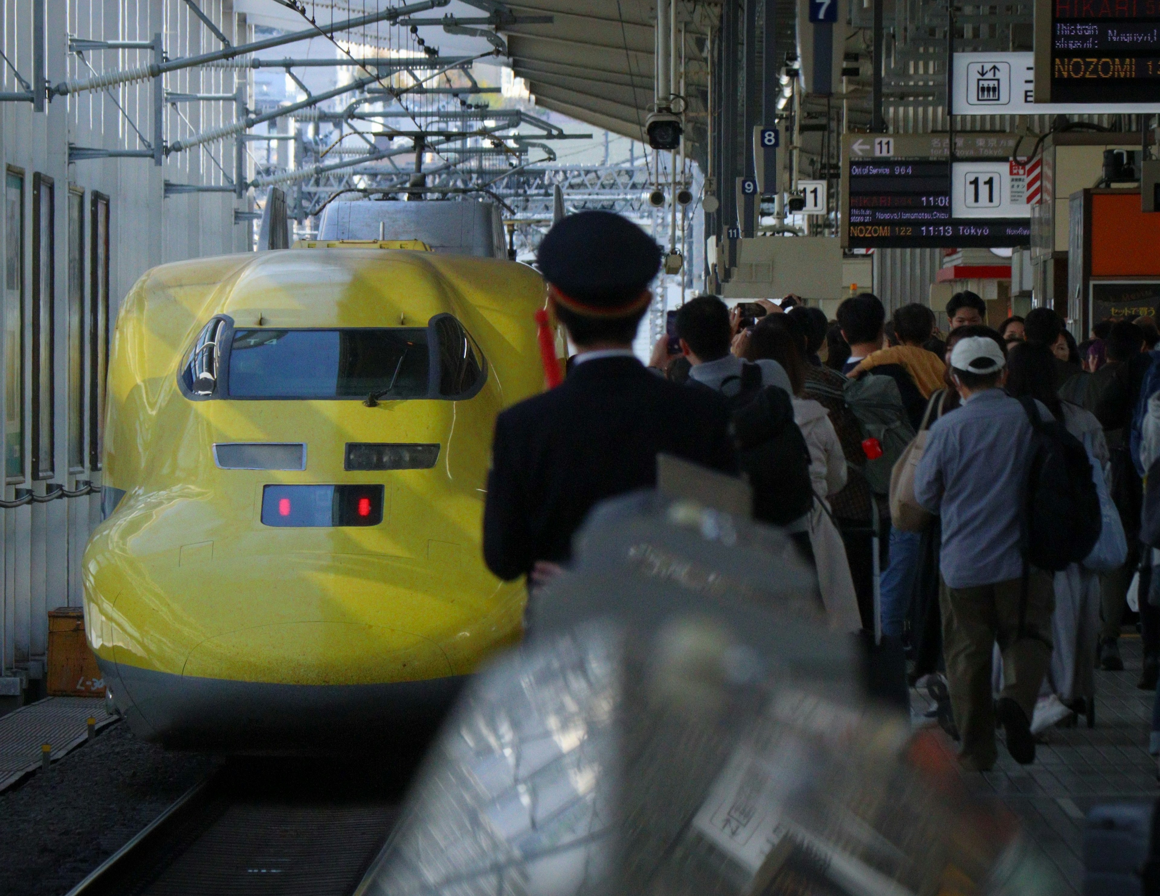 Escena de un tren Shinkansen amarillo en una estación con pasajeros esperando