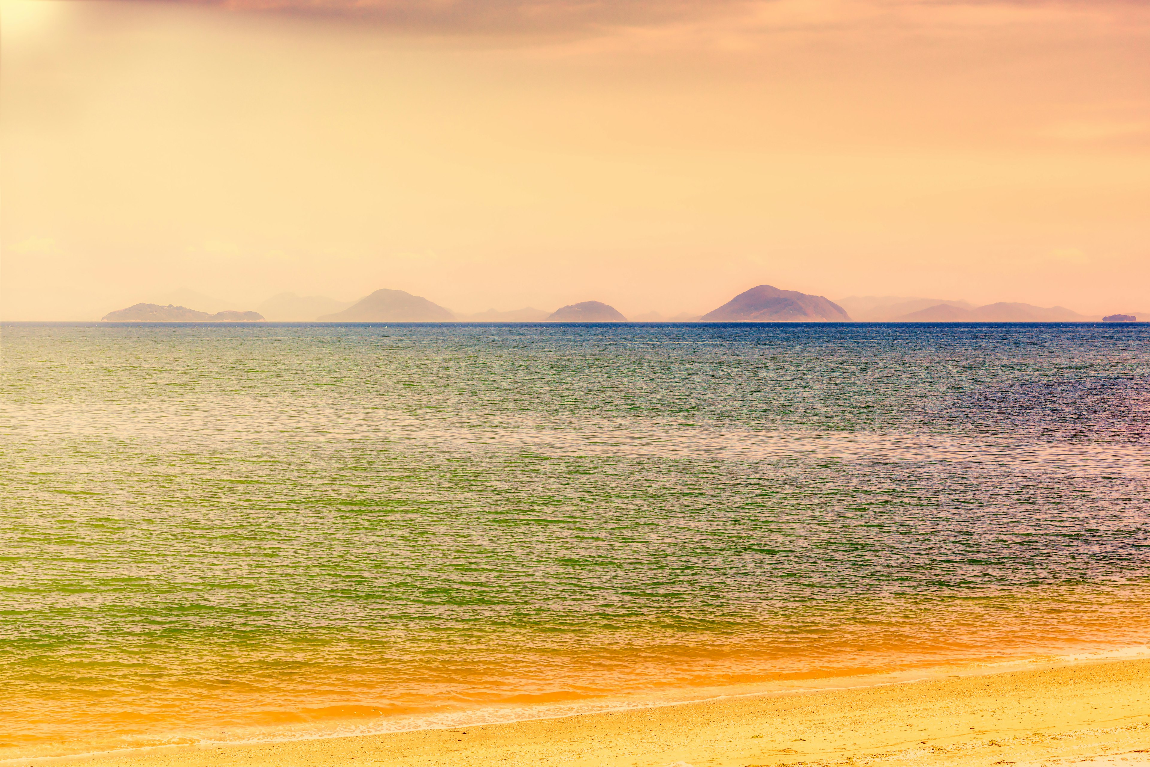 Pemandangan pantai yang tenang dengan pulau-pulau jauh di cakrawala