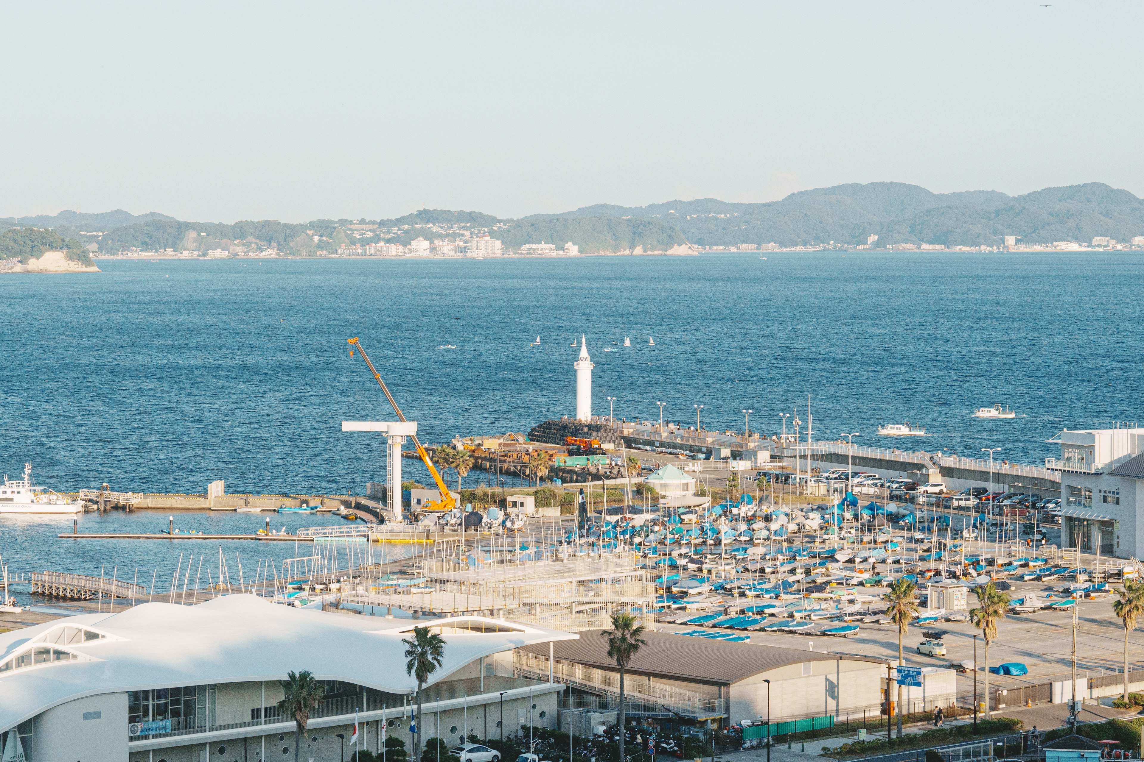 海と港の風景に浮かぶ灯台とヨットが見える