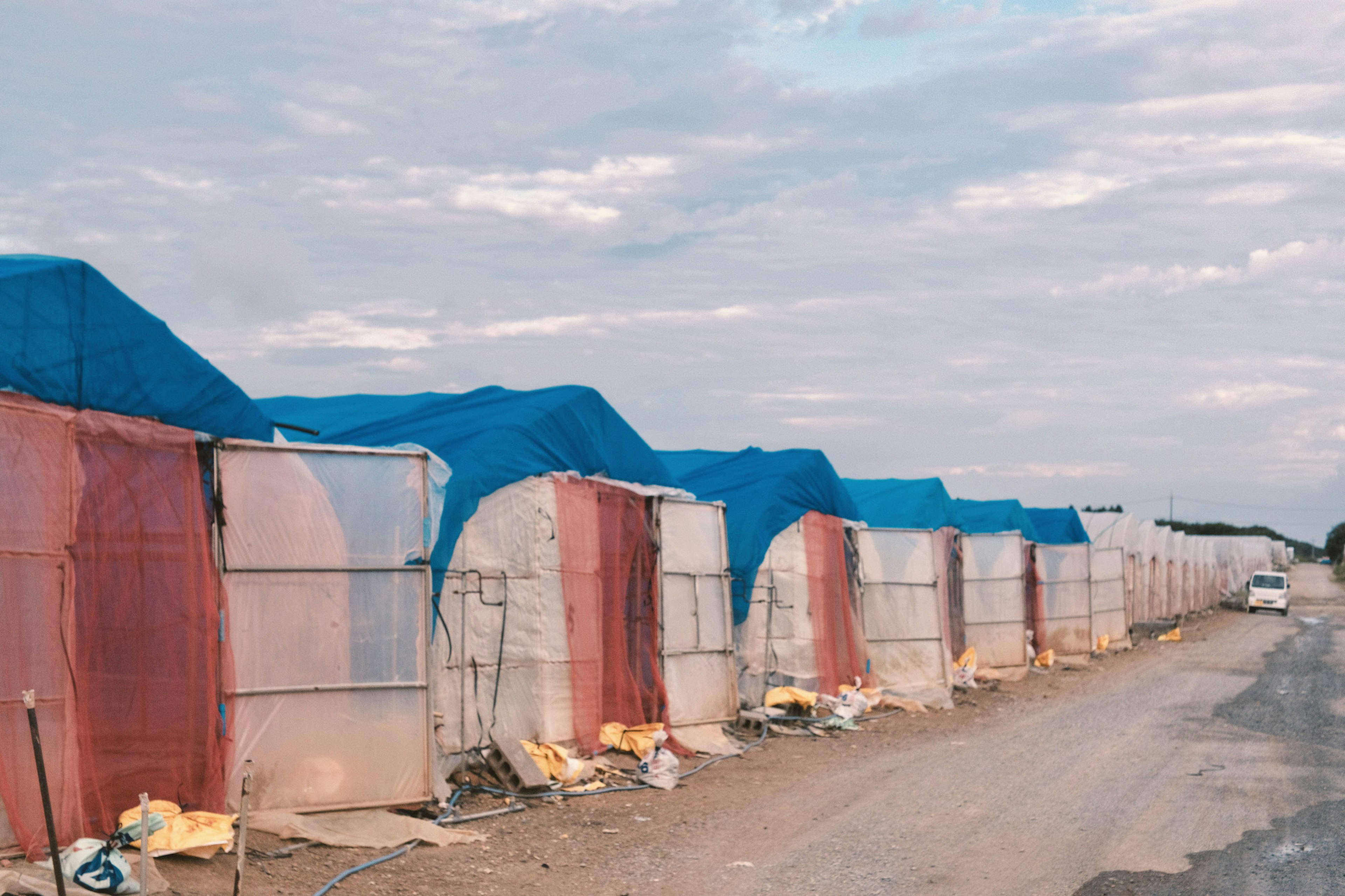 Row of tents covered with blue tarps and red fabric along a road