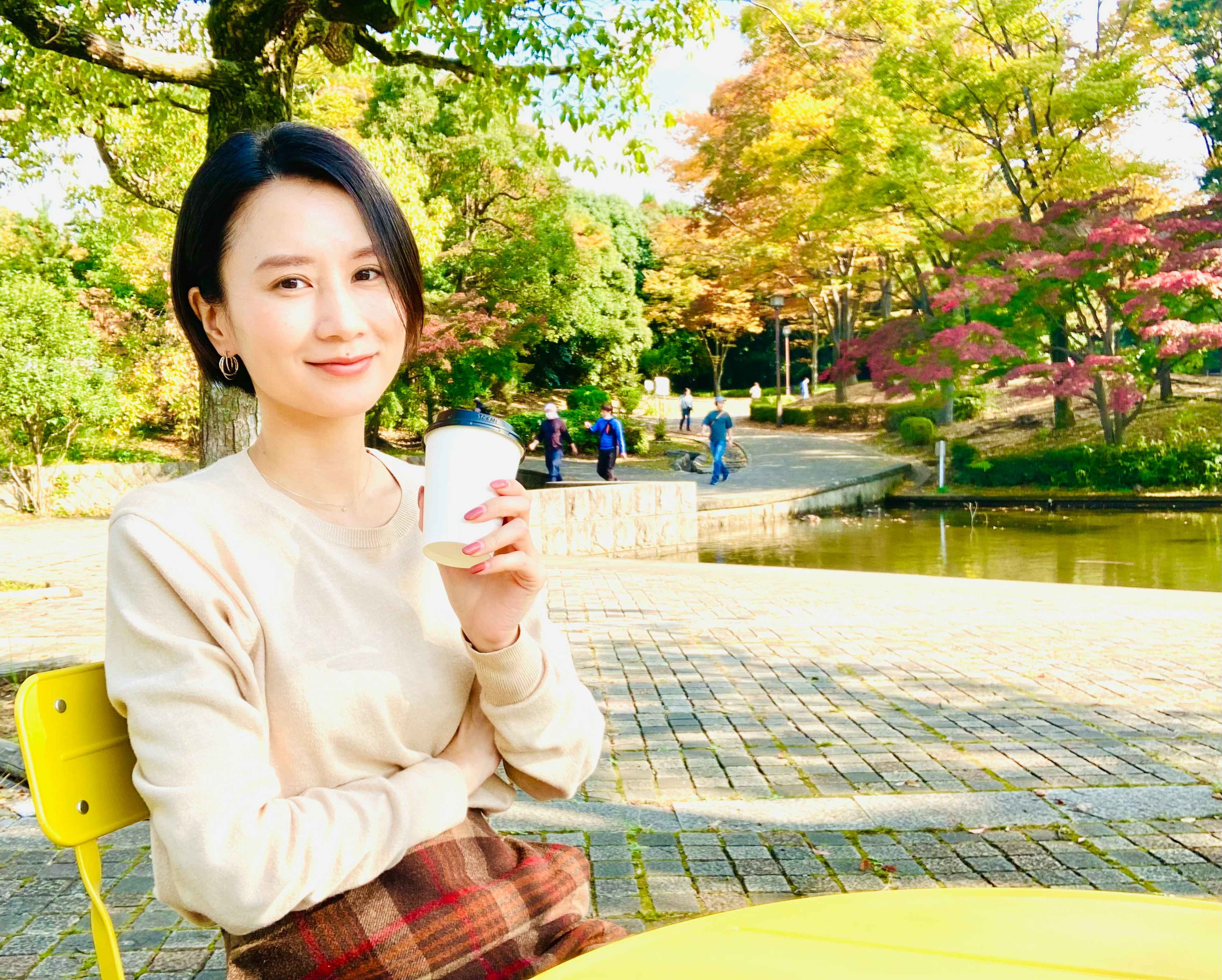 Ritratto di una donna con una tazza di caffè in un parco circondato da alberi colorati