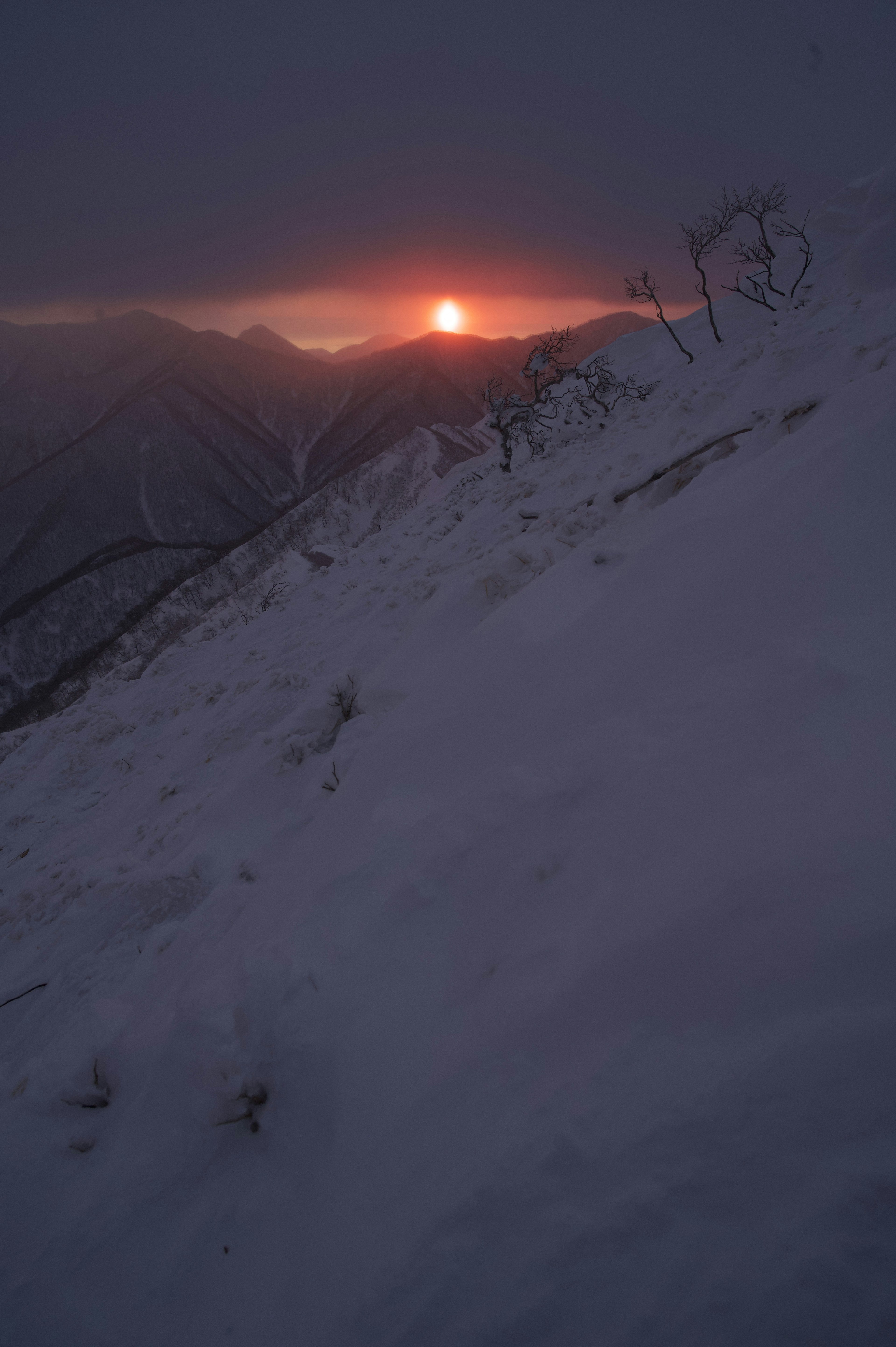 눈 덮인 산비탈 위로 지는 해와 극적인 조명