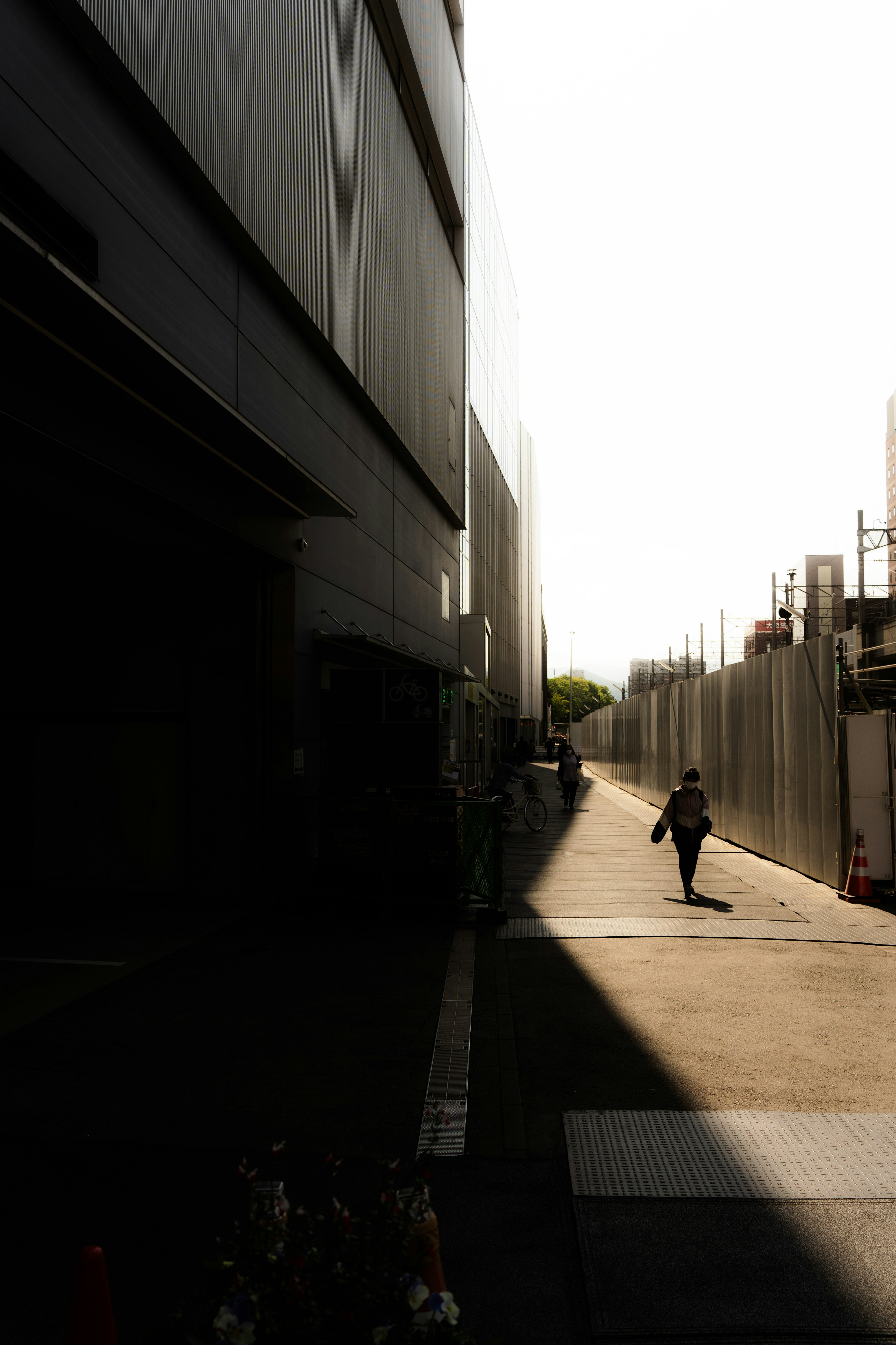 明るい背景の中を歩く人影と影のコントラストが印象的な都市の小道