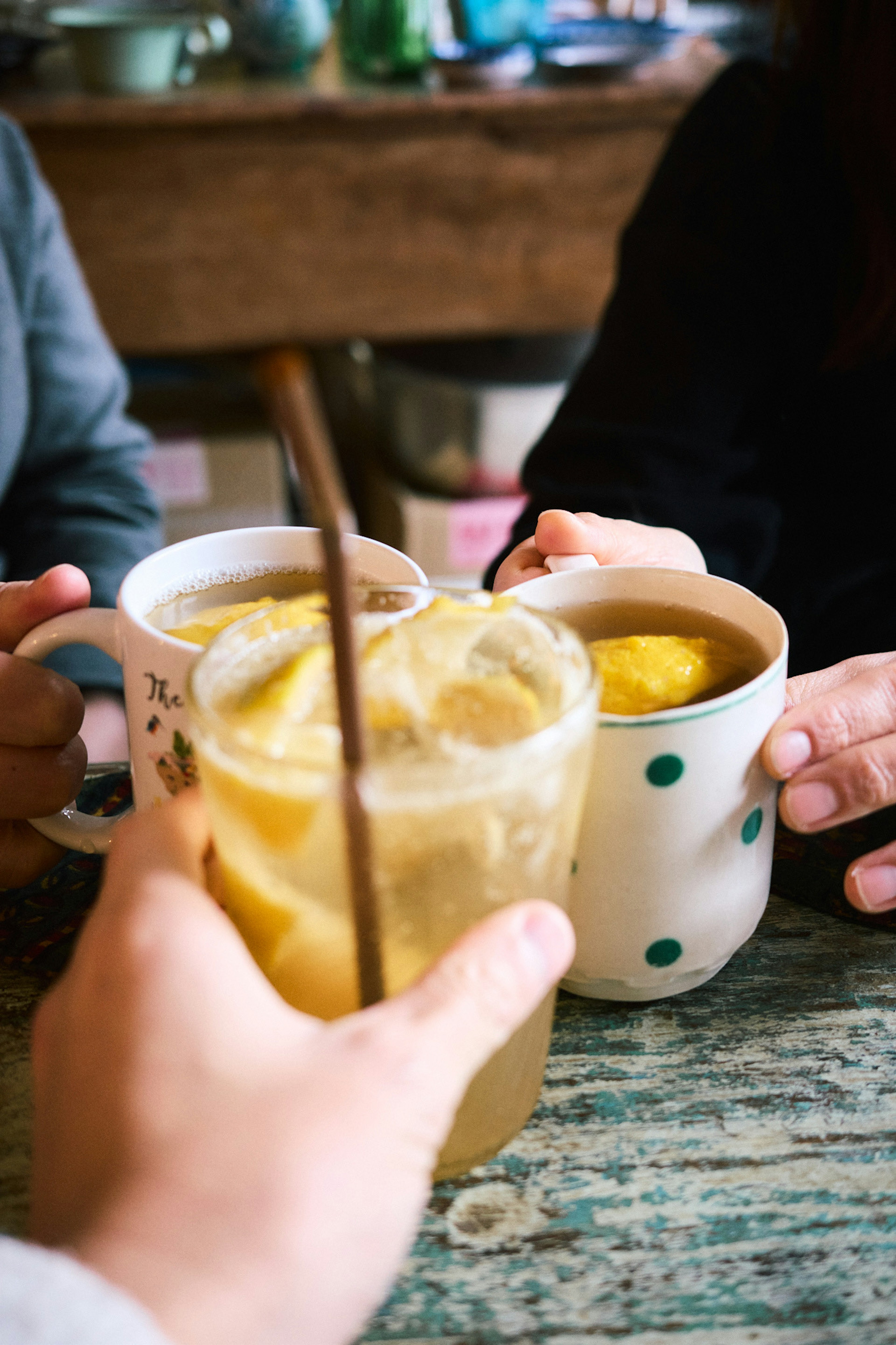 Amigos brindando con bebidas en una cafetería con una taza blanca y una taza amarilla