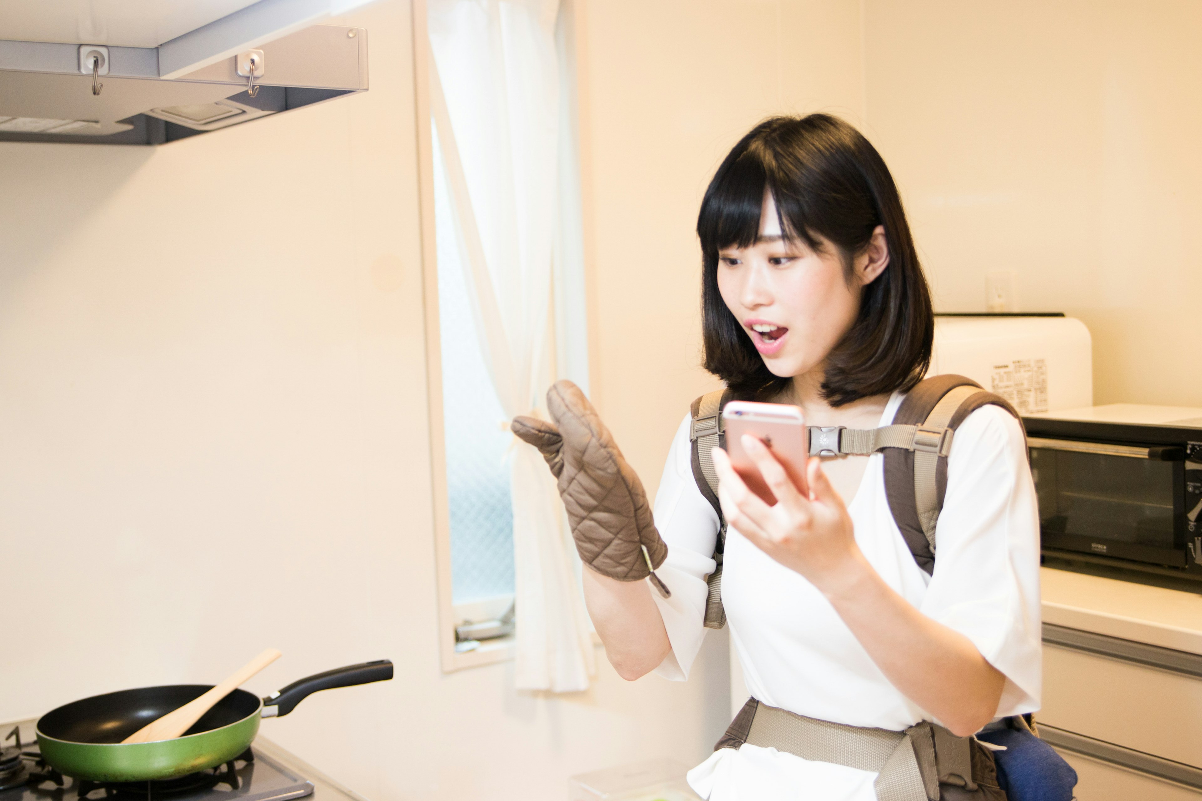 Woman cooking in the kitchen looking surprised at her smartphone