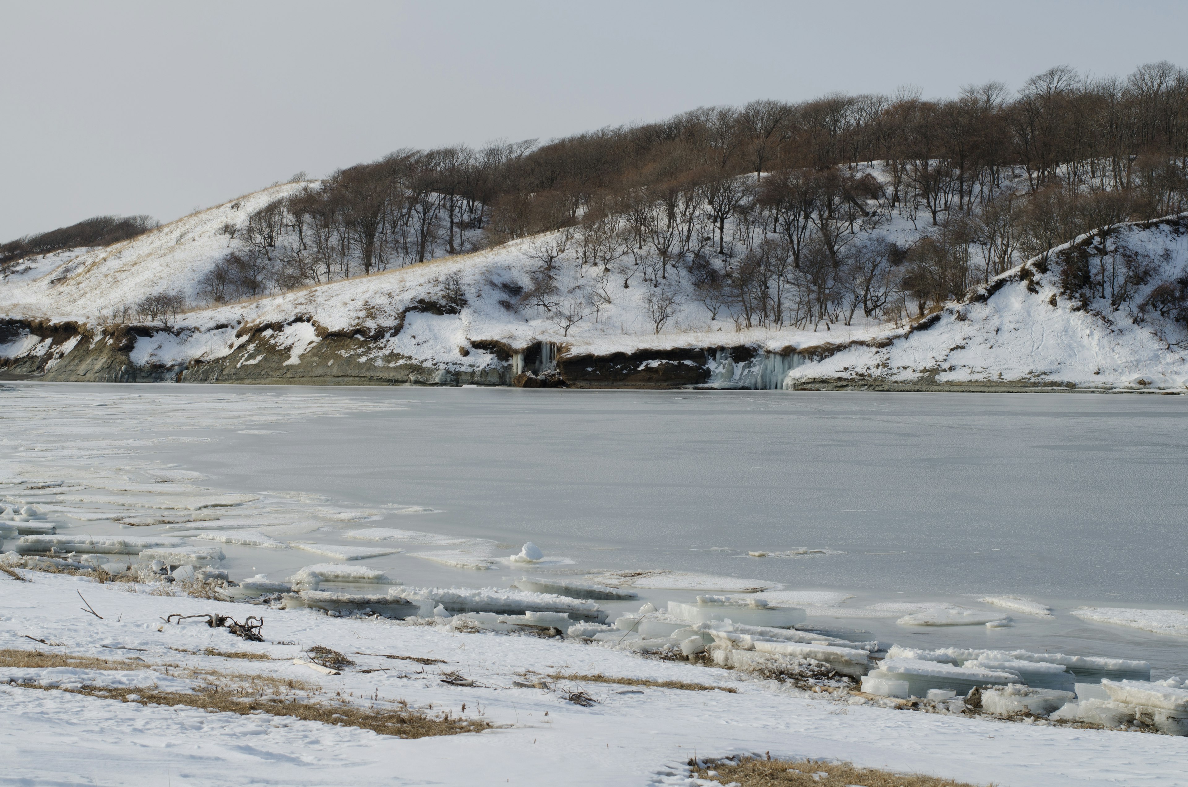 Gefrorene Flusslandschaft mit schneebedeckten Ufern und Hügeln im Winter