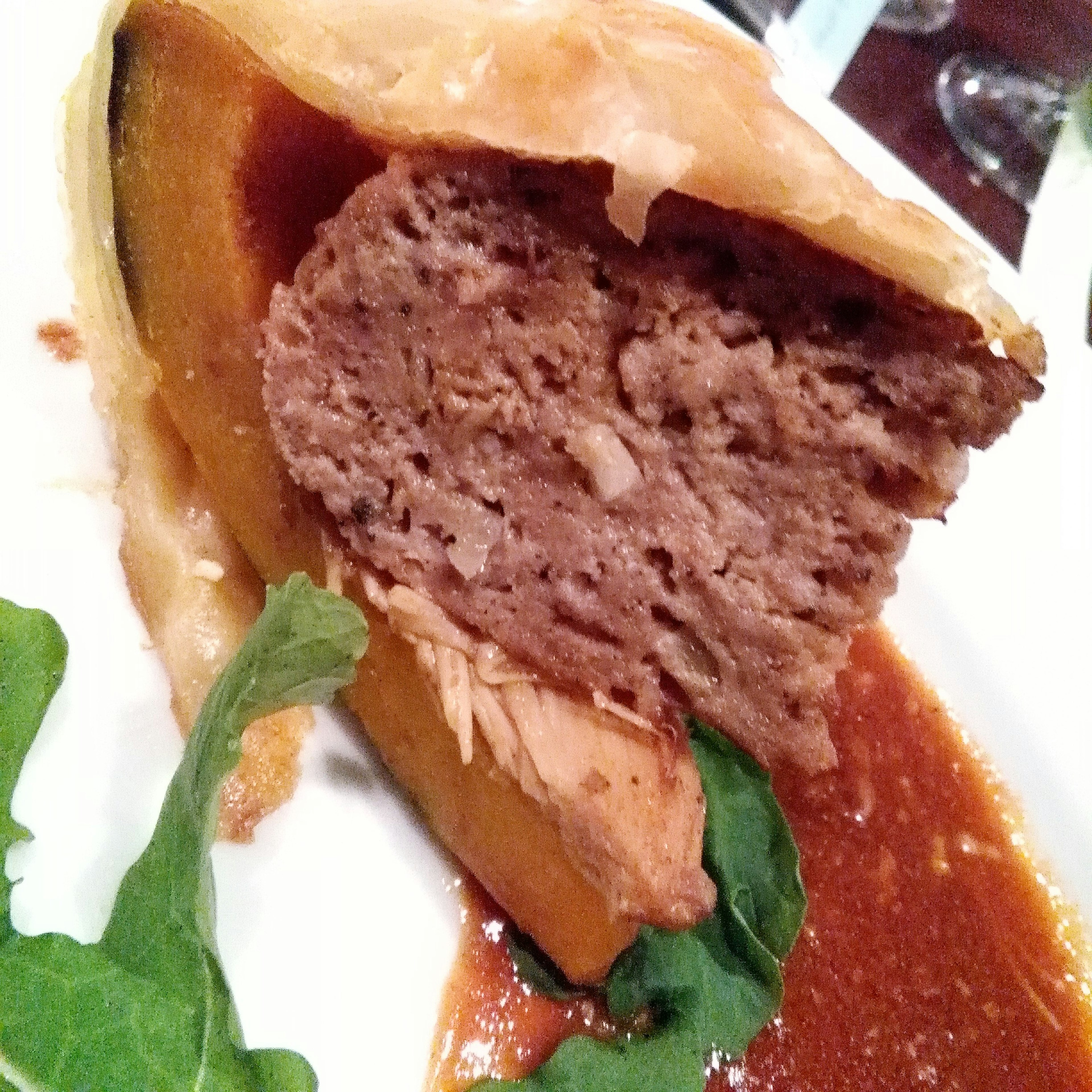 Slice of meat dish wrapped in pastry with sauce and greens