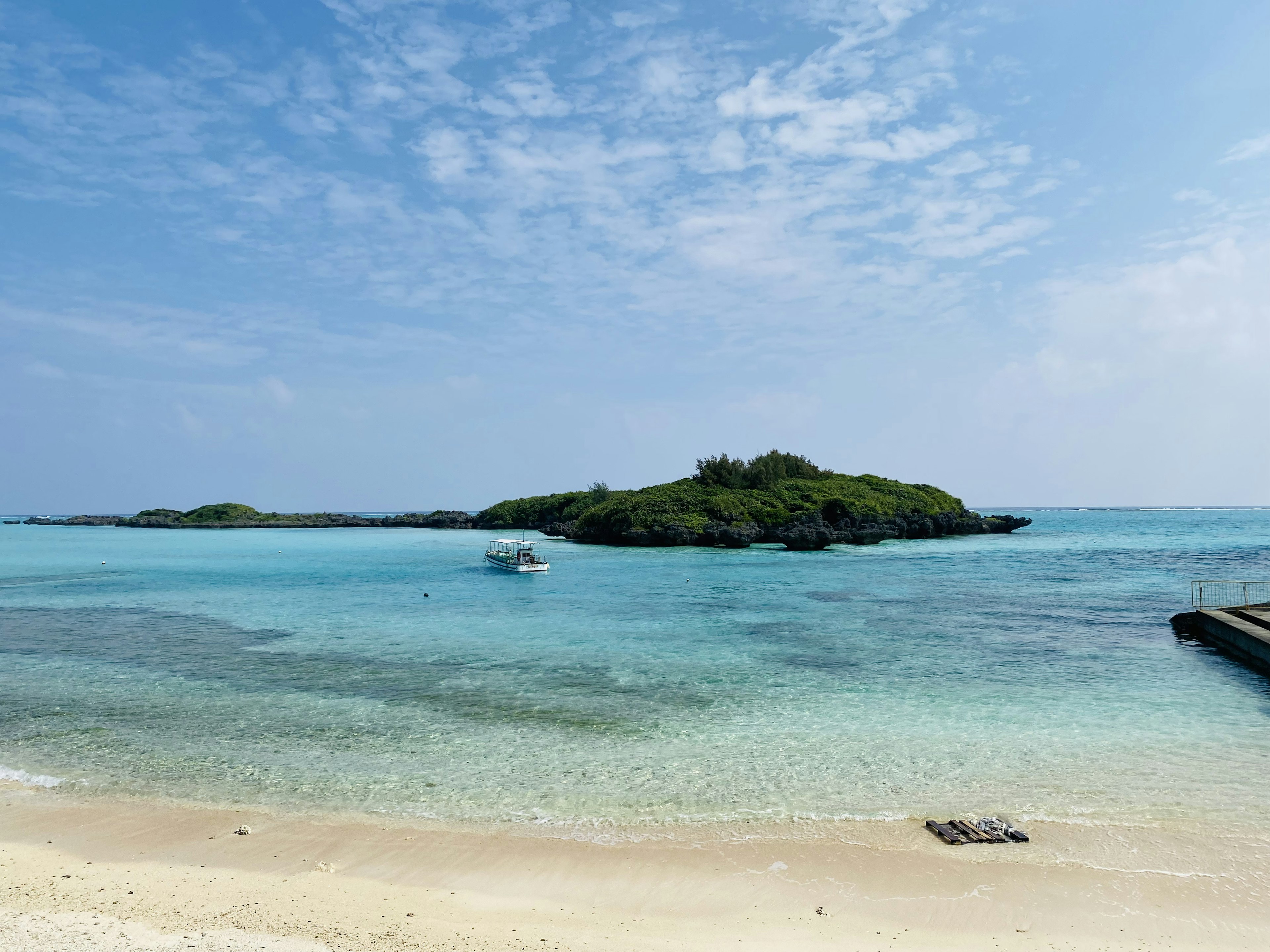 Vista escénica de agua turquesa y playa de arena con una pequeña isla y un bote