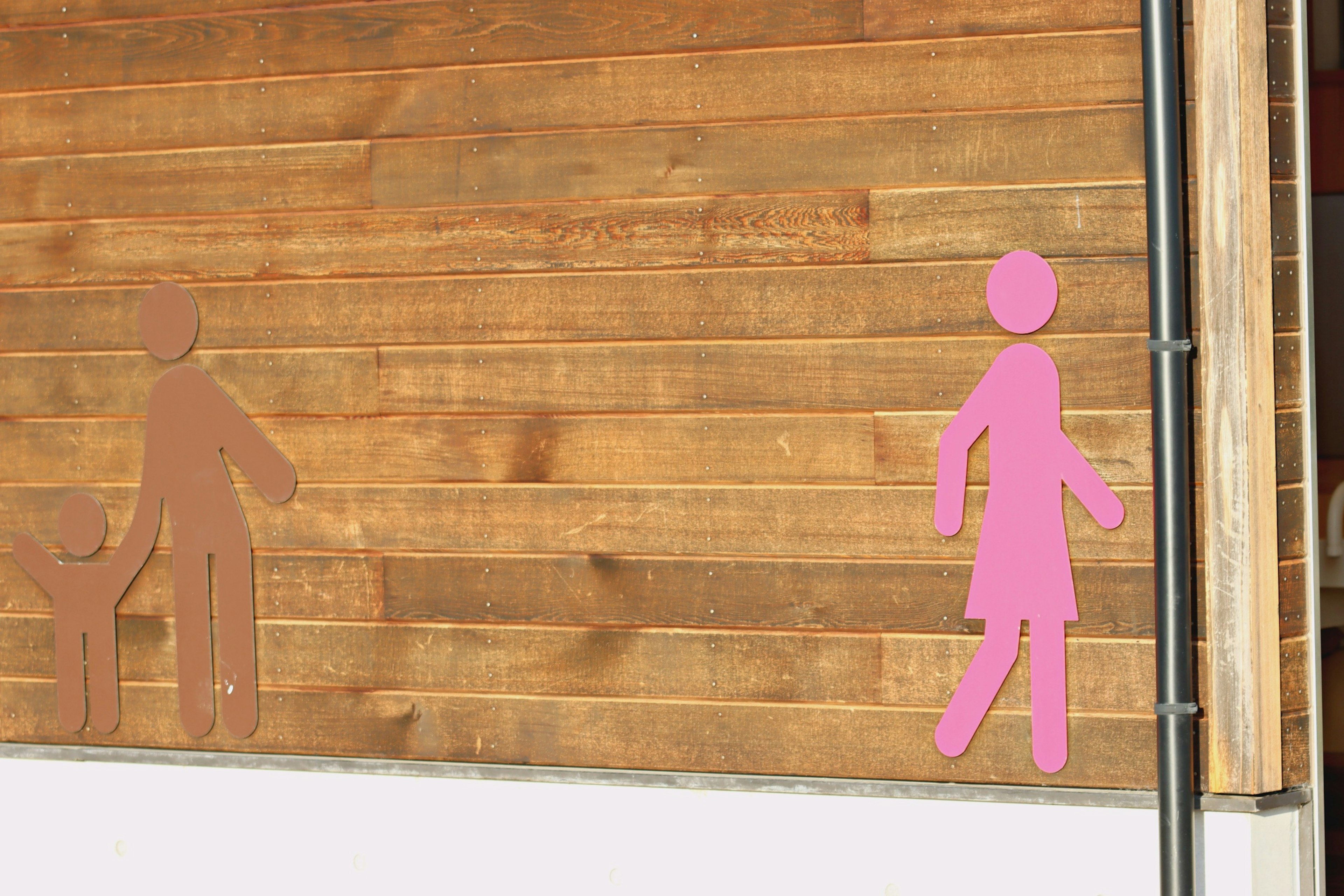 Silhouette di una figura femminile rosa e di una figura maschile marrone su un muro di legno