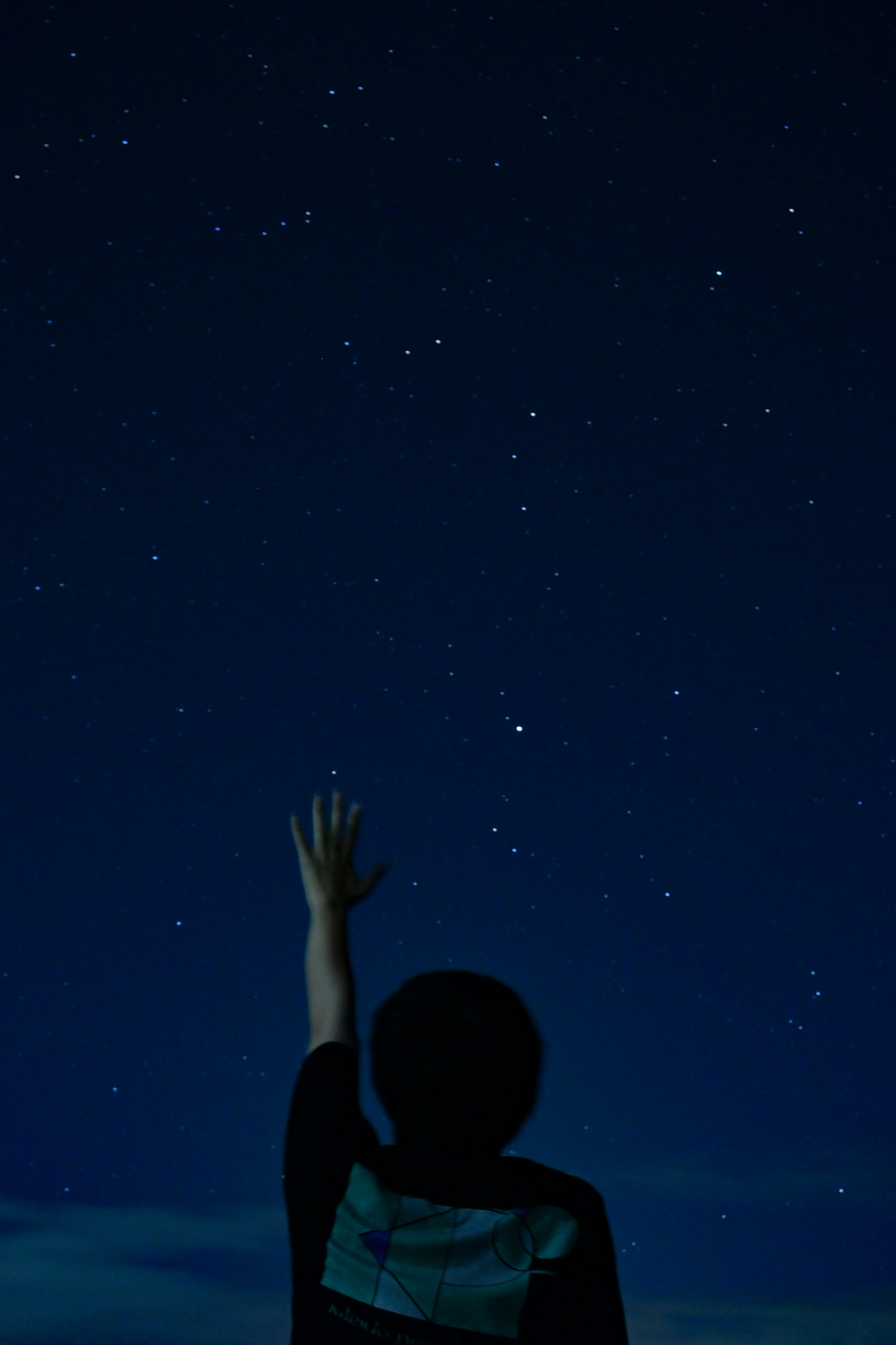 Silhouette d'un garçon tendant la main vers les étoiles dans un ciel nocturne
