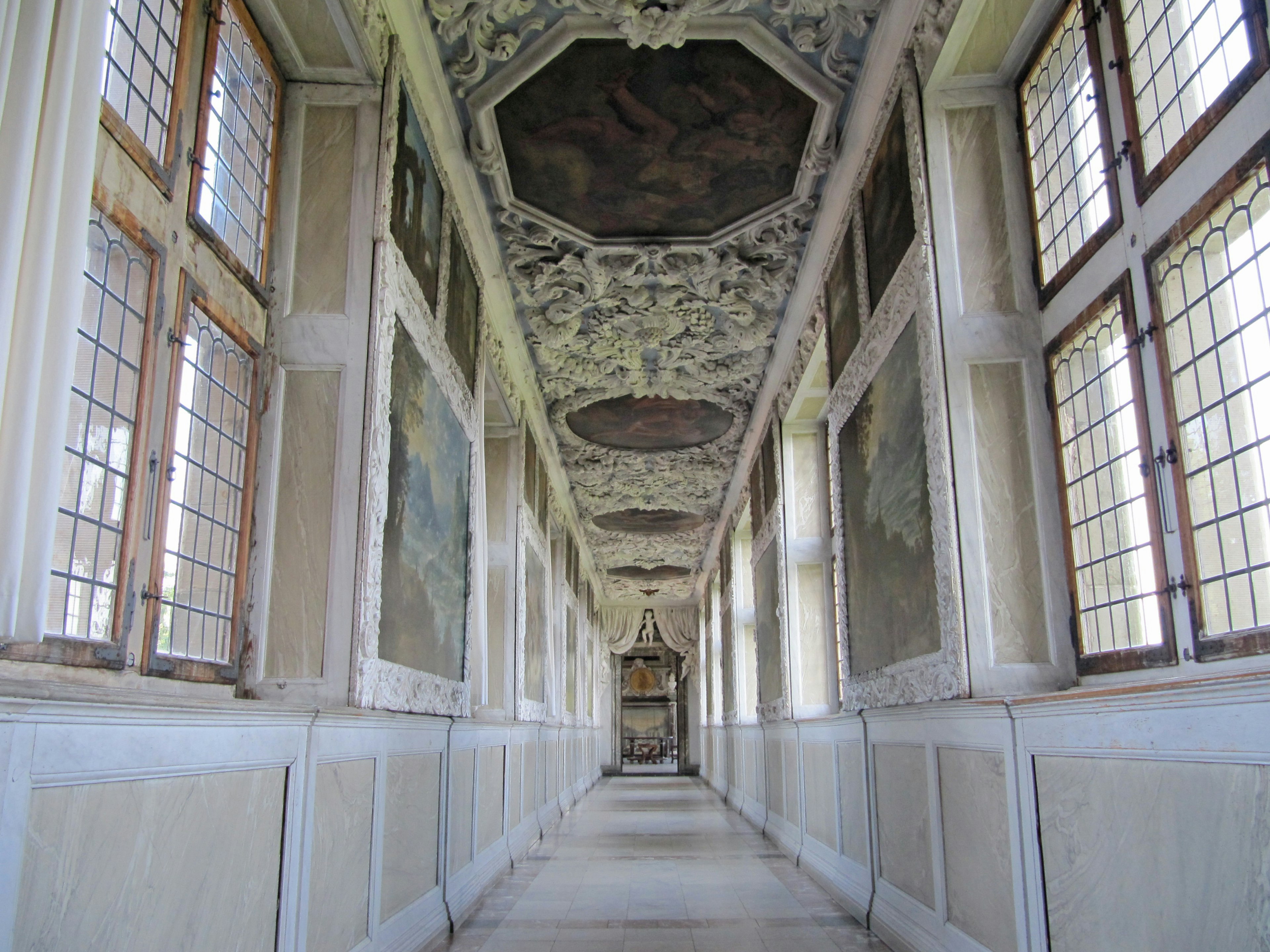 Long couloir intérieur avec des murs peints en fresque et lumière naturelle des fenêtres