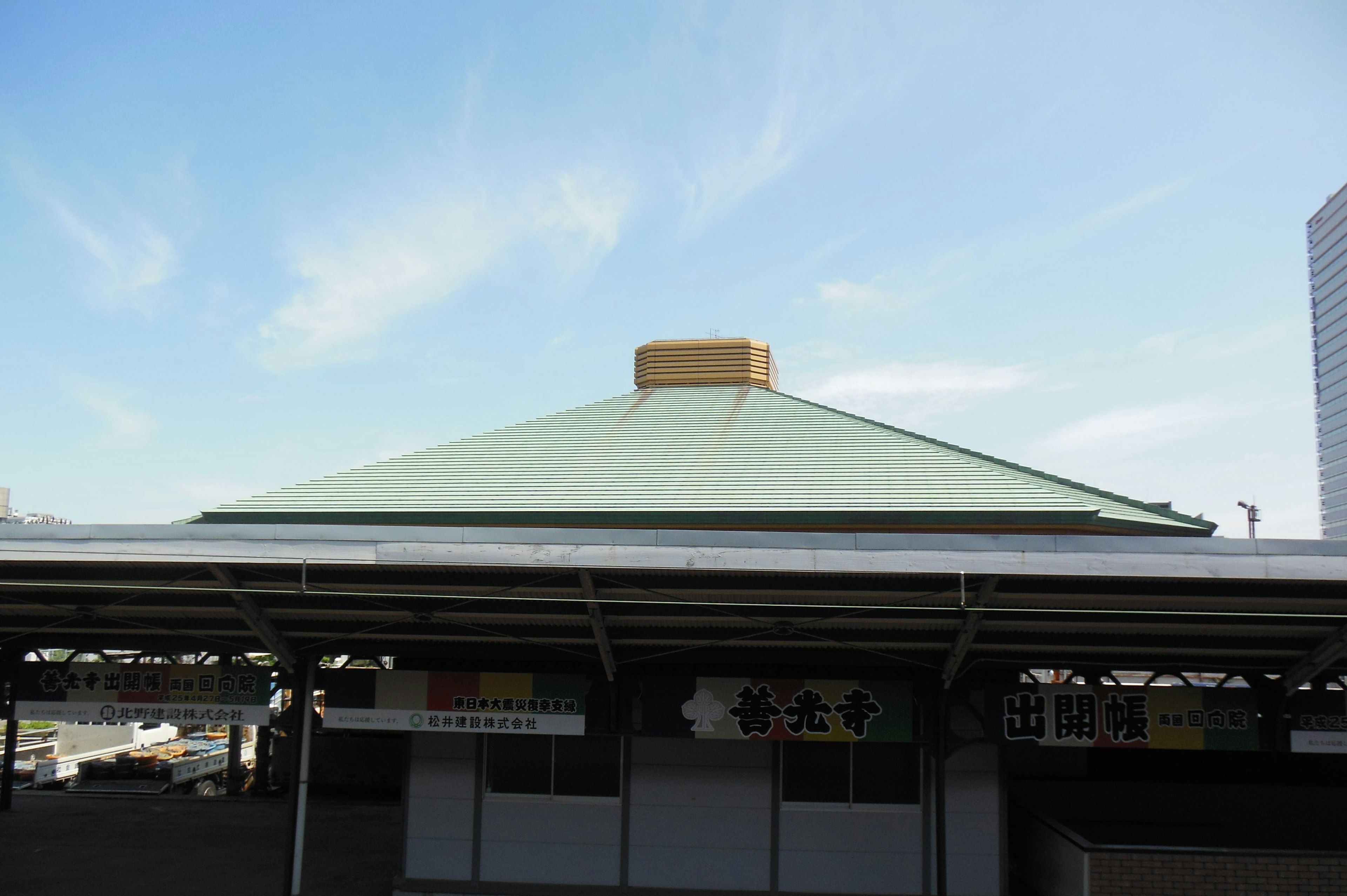 Building with a green roof under a blue sky featuring a distinctive peaked top and a golden ornament