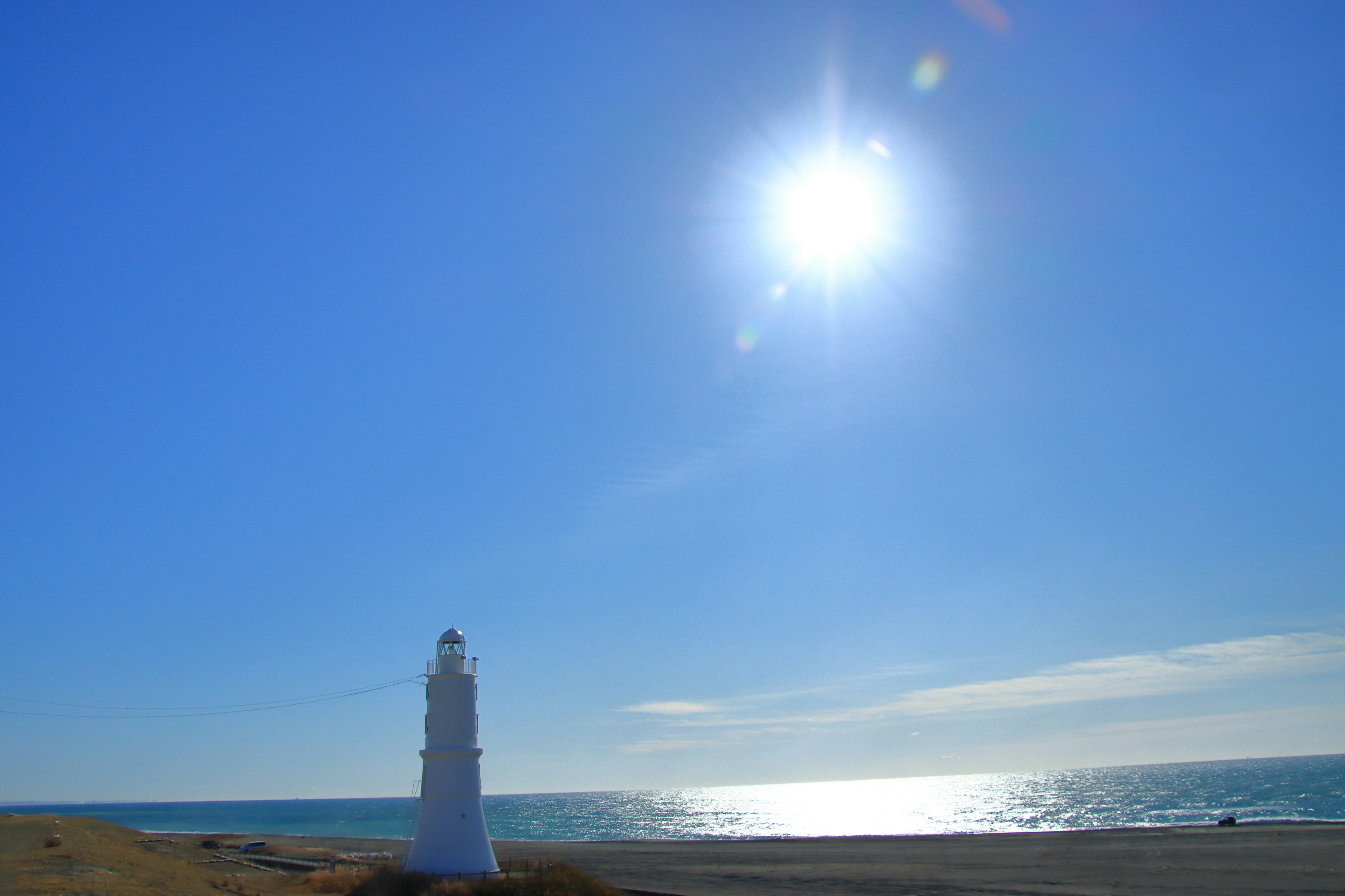 Faro bianco su una spiaggia con cielo blu e oceano