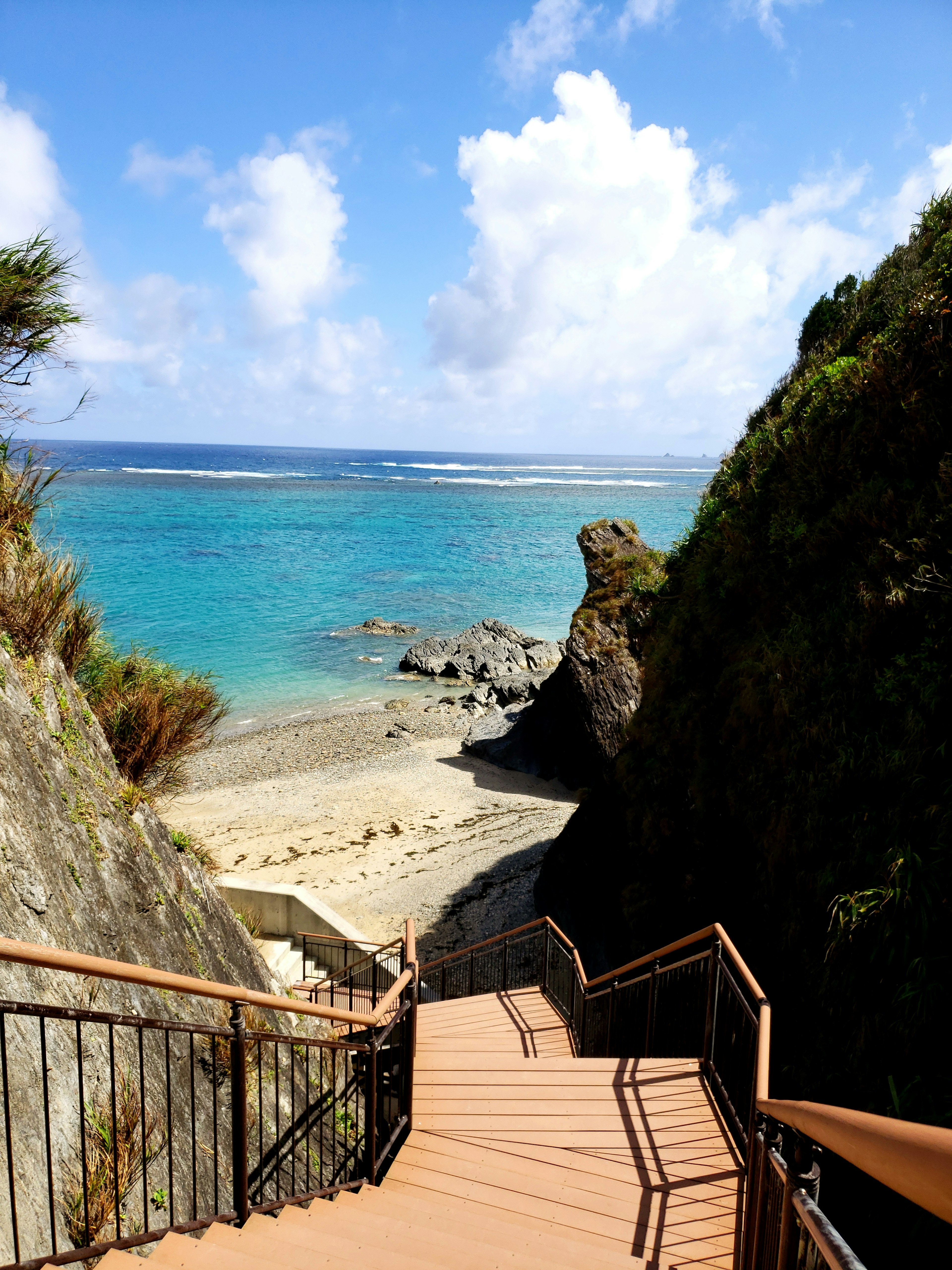 Escaleras que conducen a una playa con agua turquesa y cielo azul