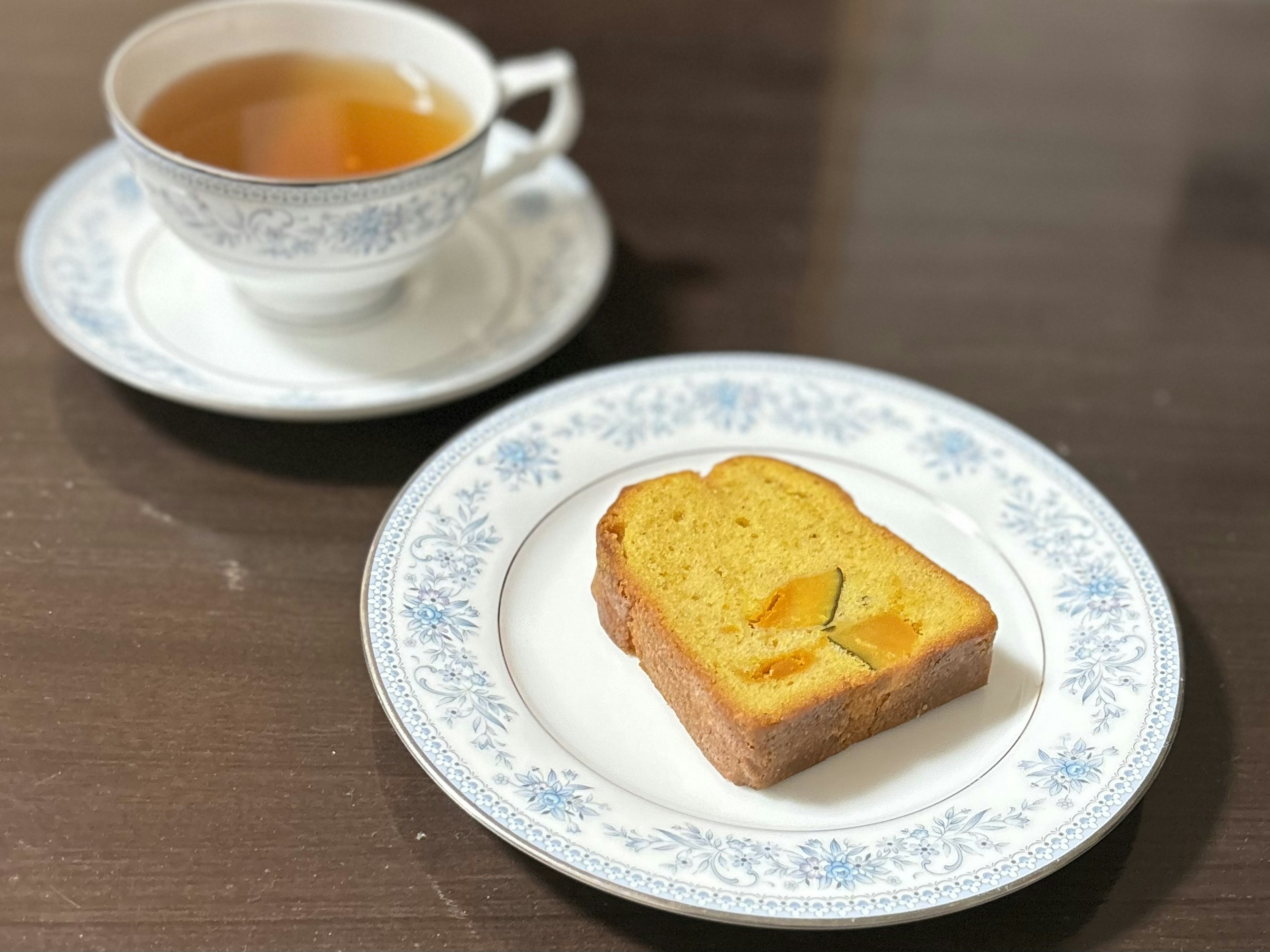 Imagen de una taza de té y una rebanada de pastel de naranja en un plato decorativo