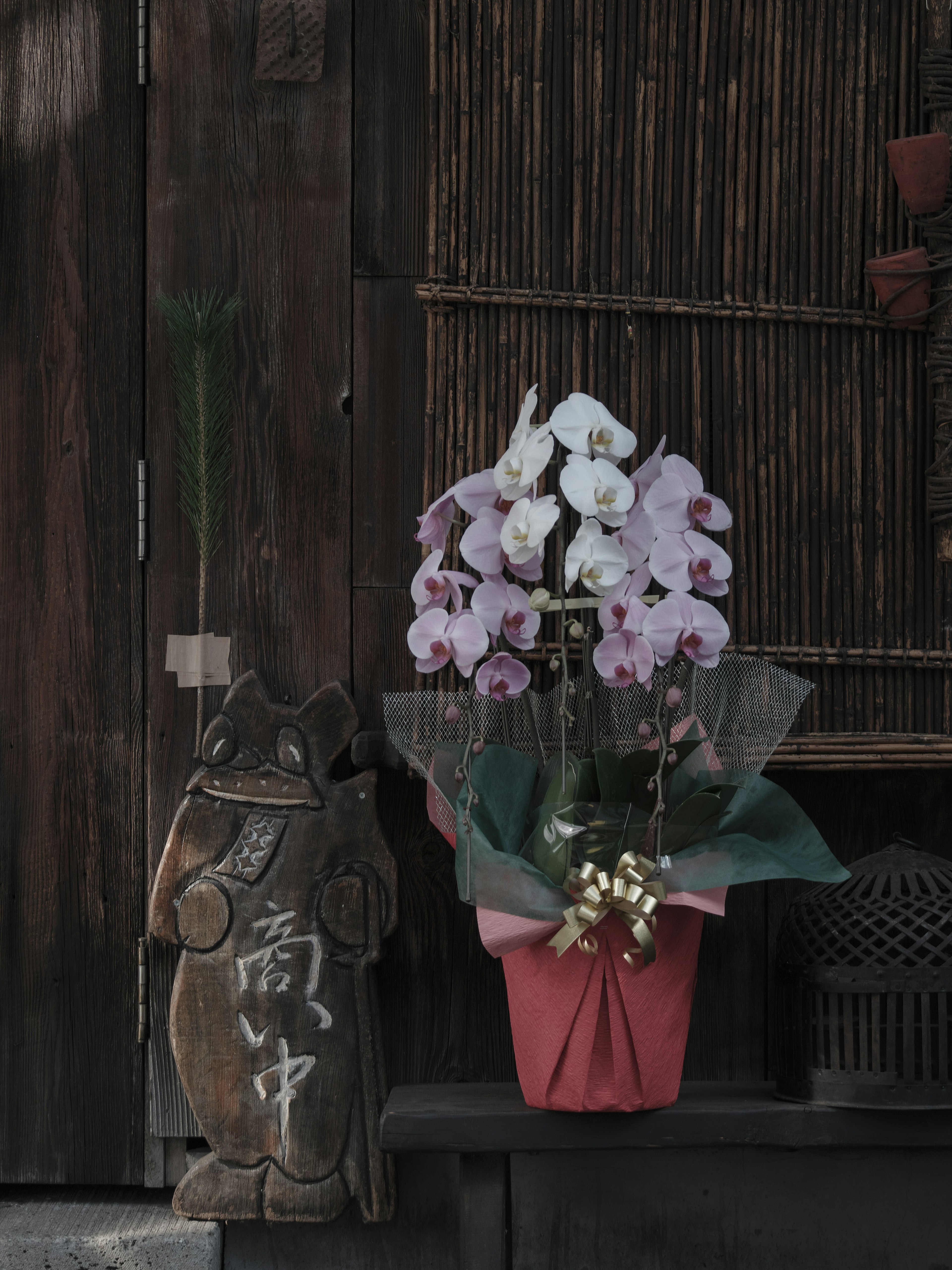 Pink orchid bouquet in a pot beside a ceramic decoration against a wooden background