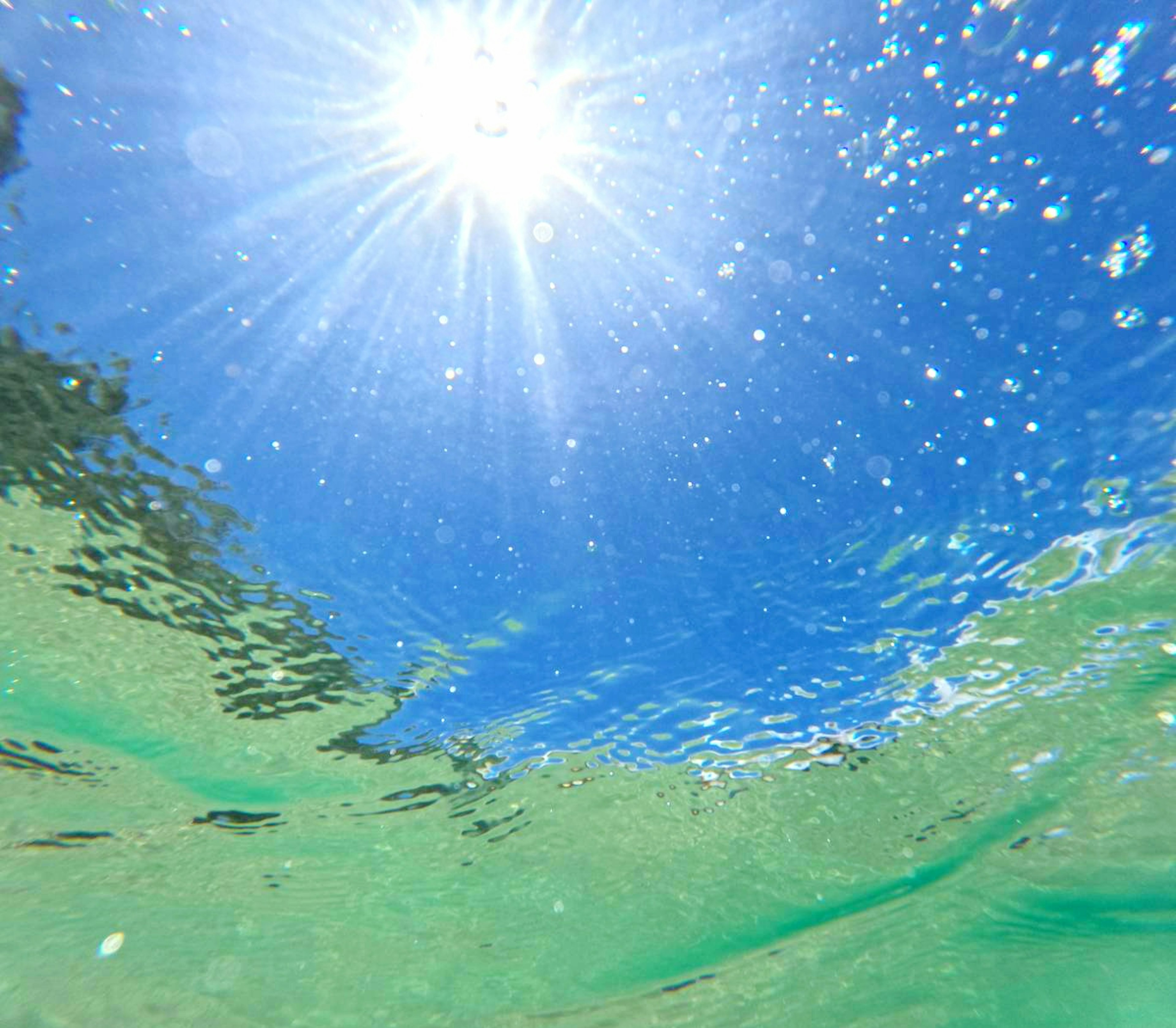 Unterwasseransicht mit hellem Sonnenlicht und blauem Himmel, der sich auf der Wasseroberfläche spiegelt