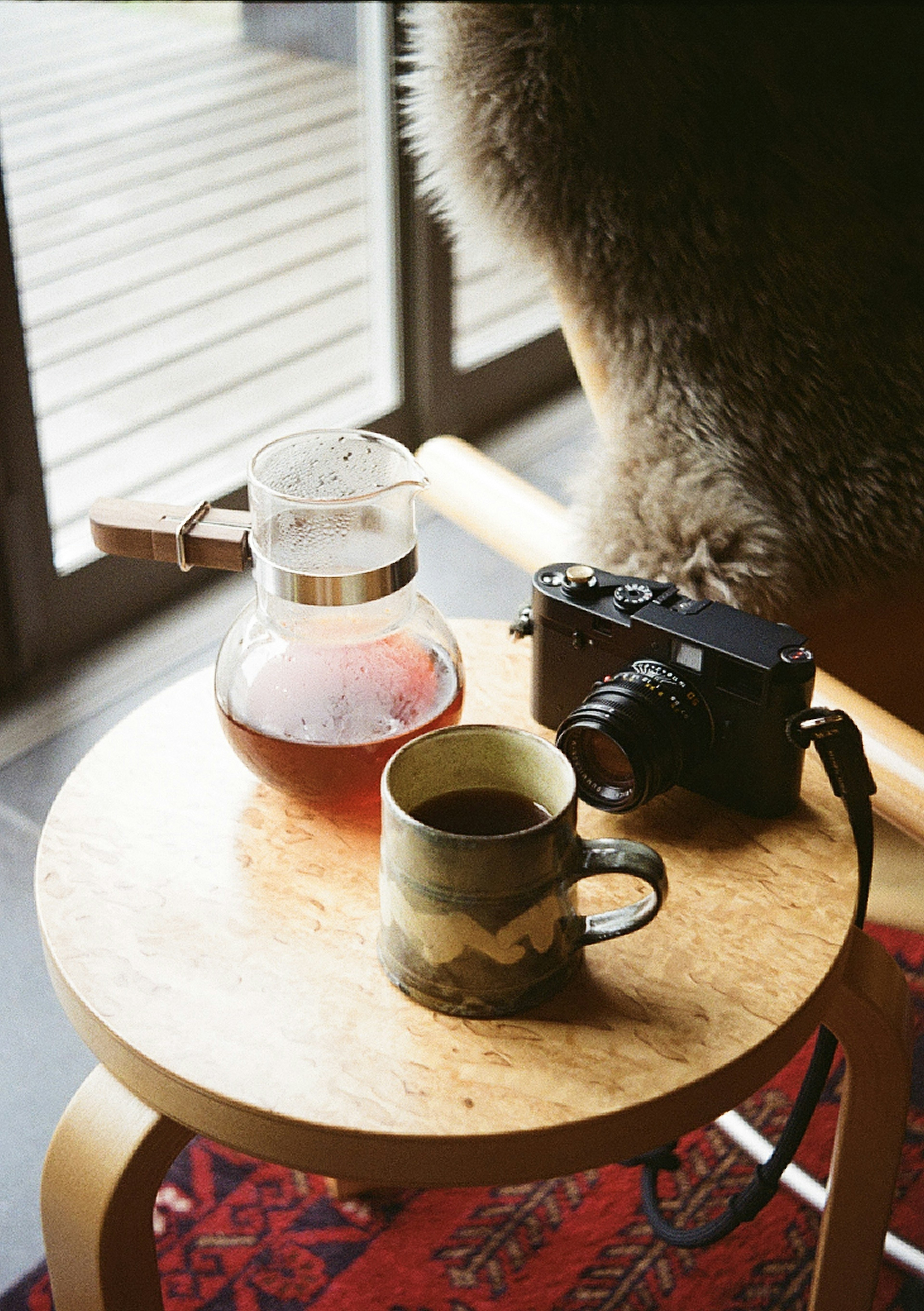 A wooden table featuring a coffee pot and a camera