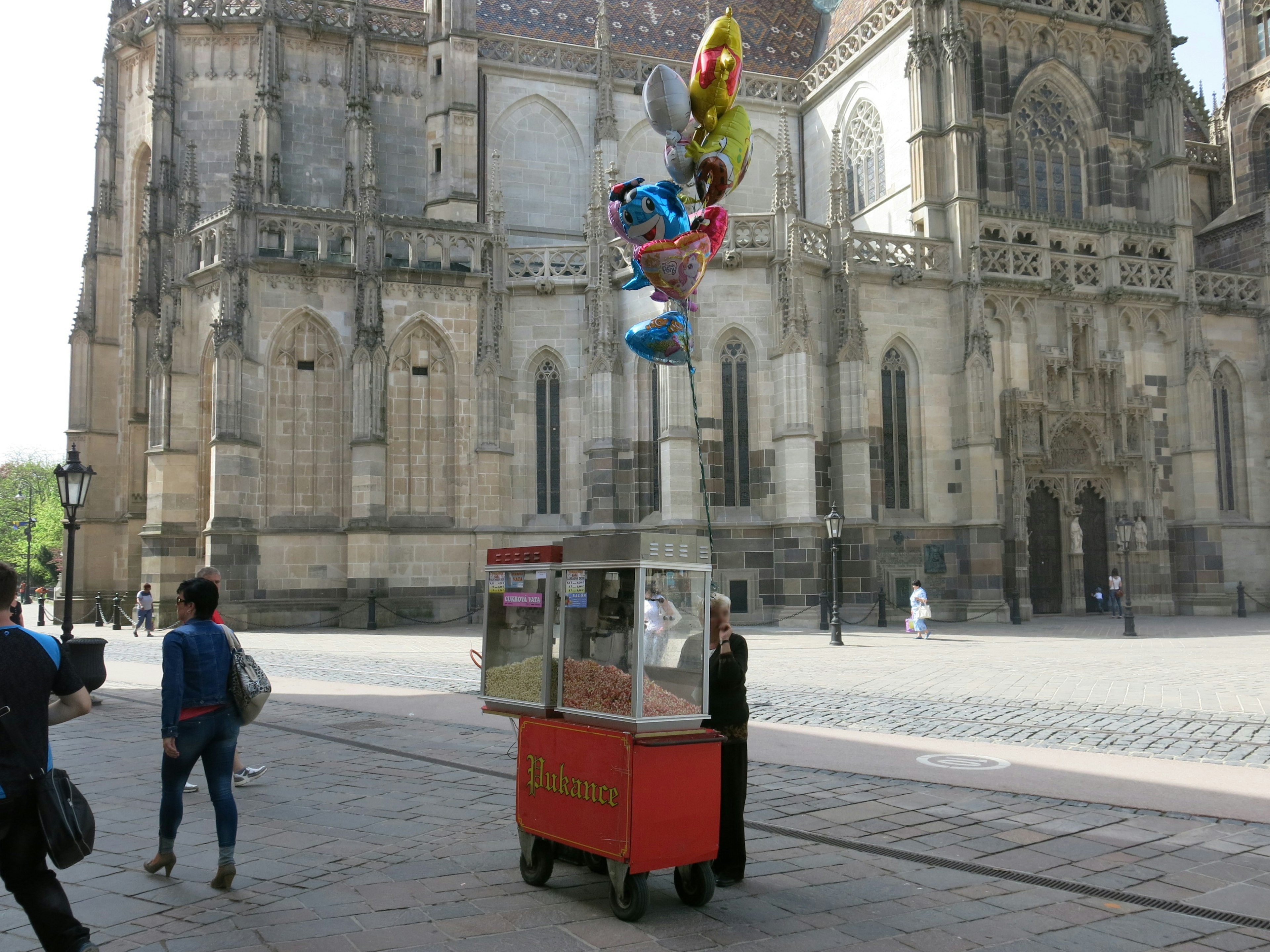 Chariot de vente de ballons près d'une cathédrale avec des piétons