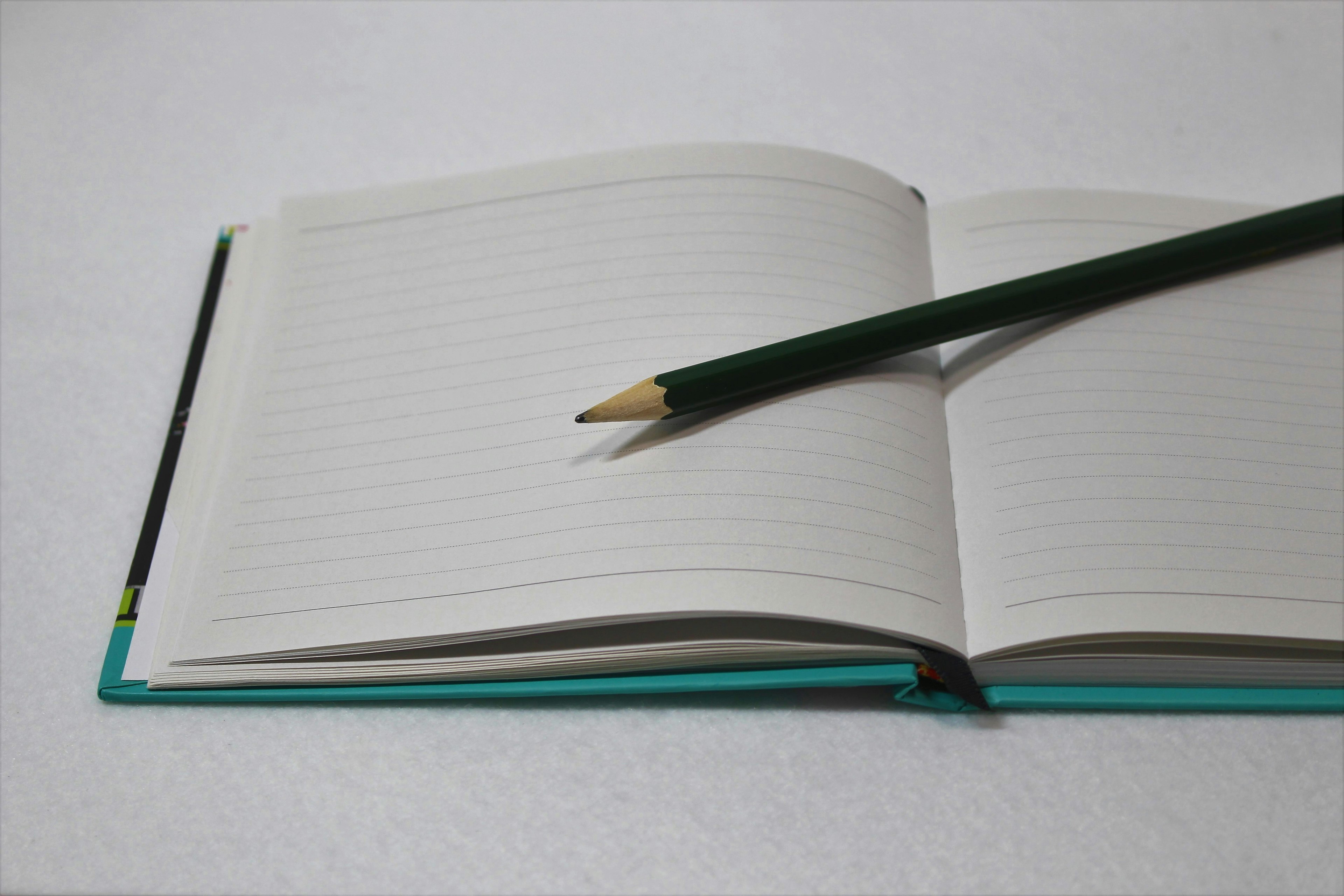 An open notebook with blank pages and a green pencil resting on it