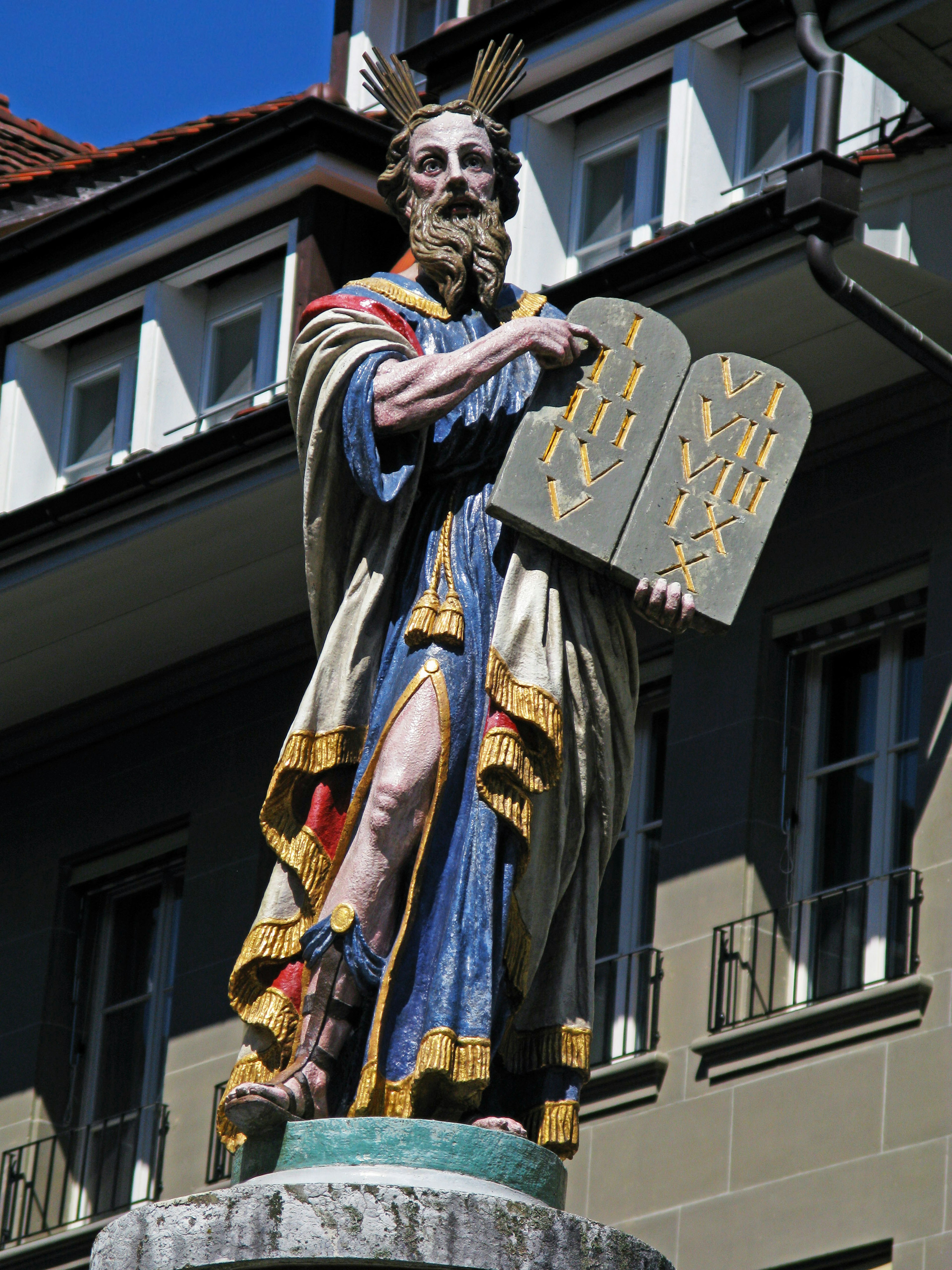 Eine bunte Statue eines Heiligen, der zwei Steintafeln hält, steht im Vordergrund