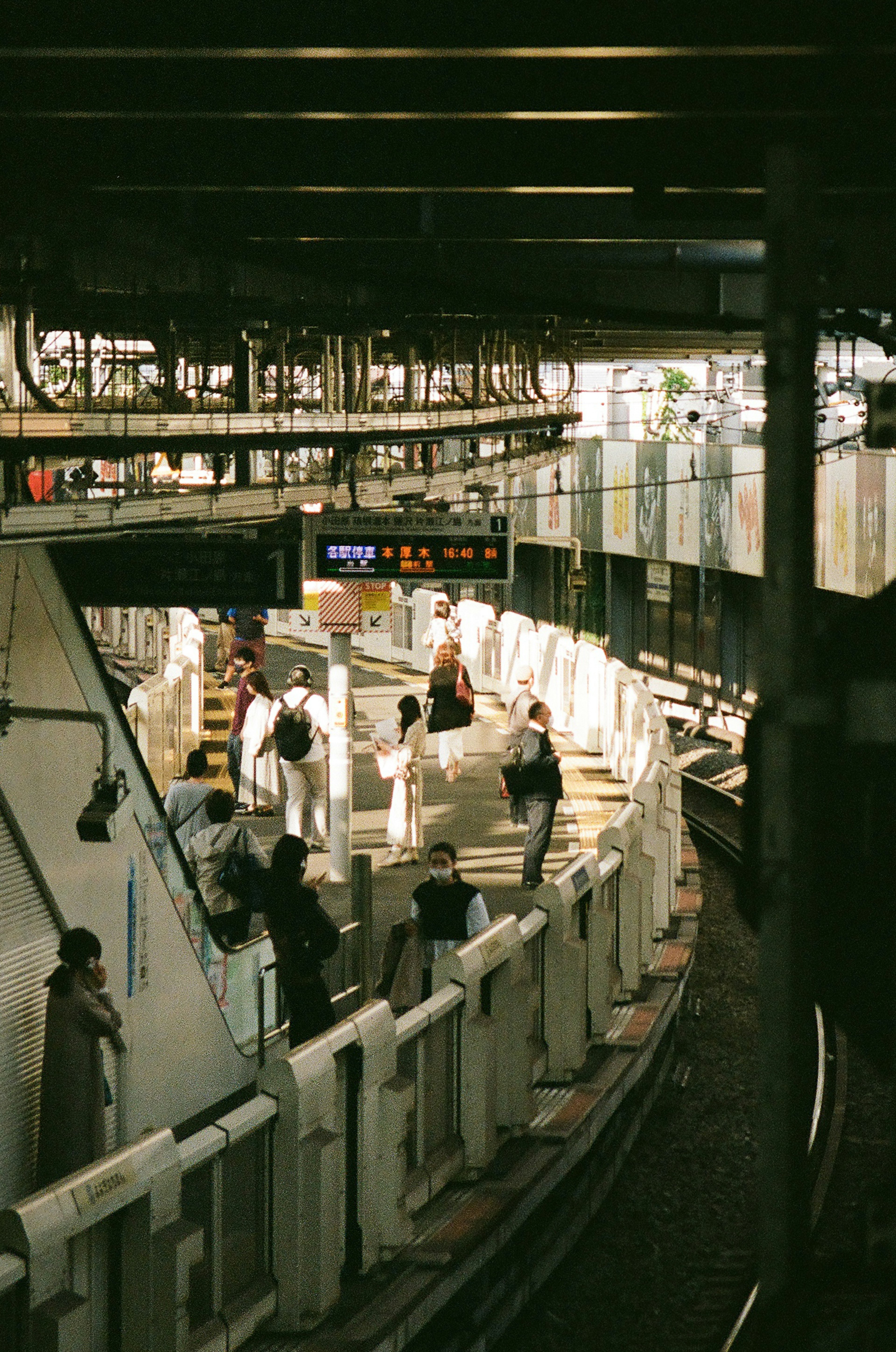 View of a train station platform with curved tracks featuring several passengers and display boards