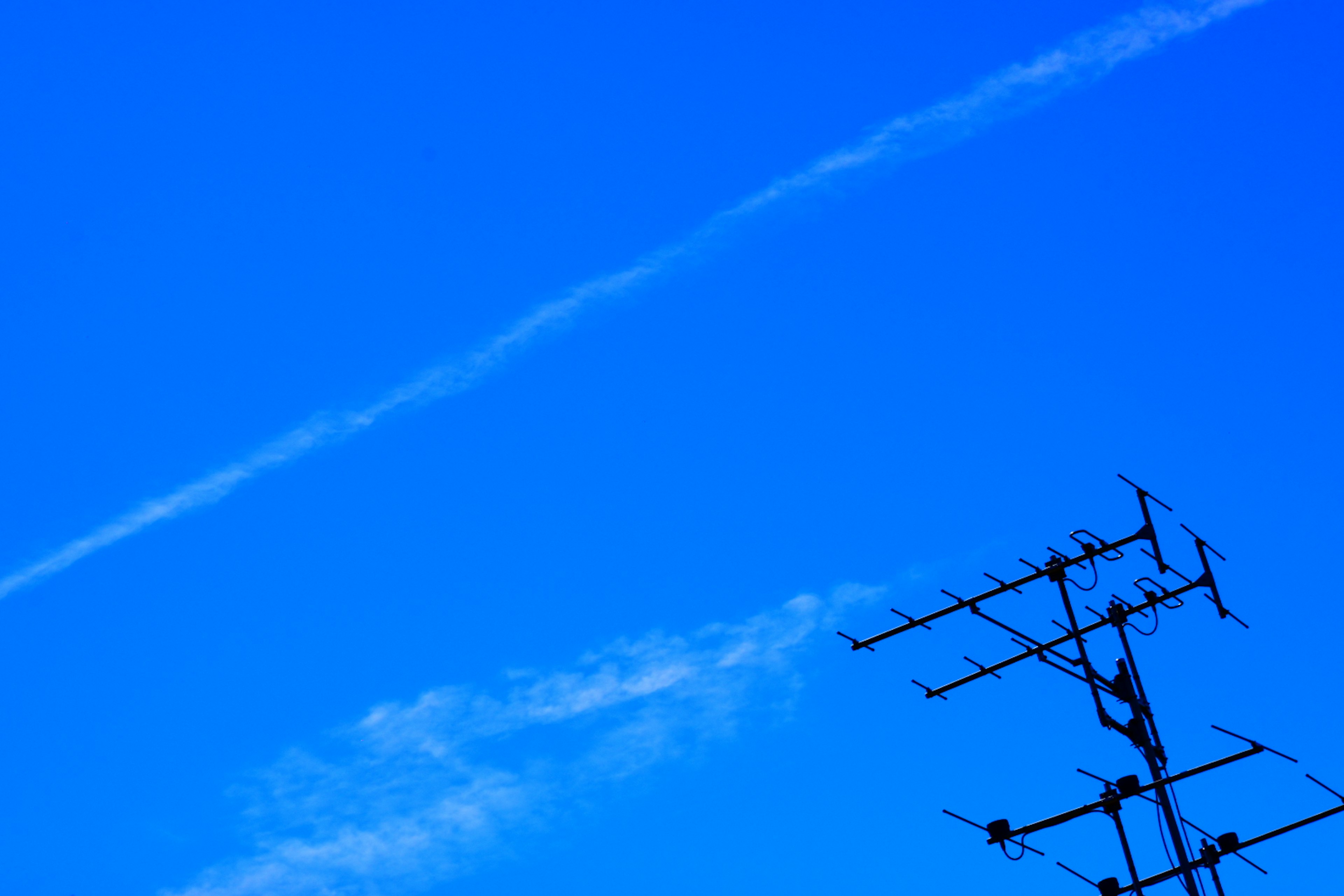 Antenna silhouetted against a bright blue sky with wispy clouds