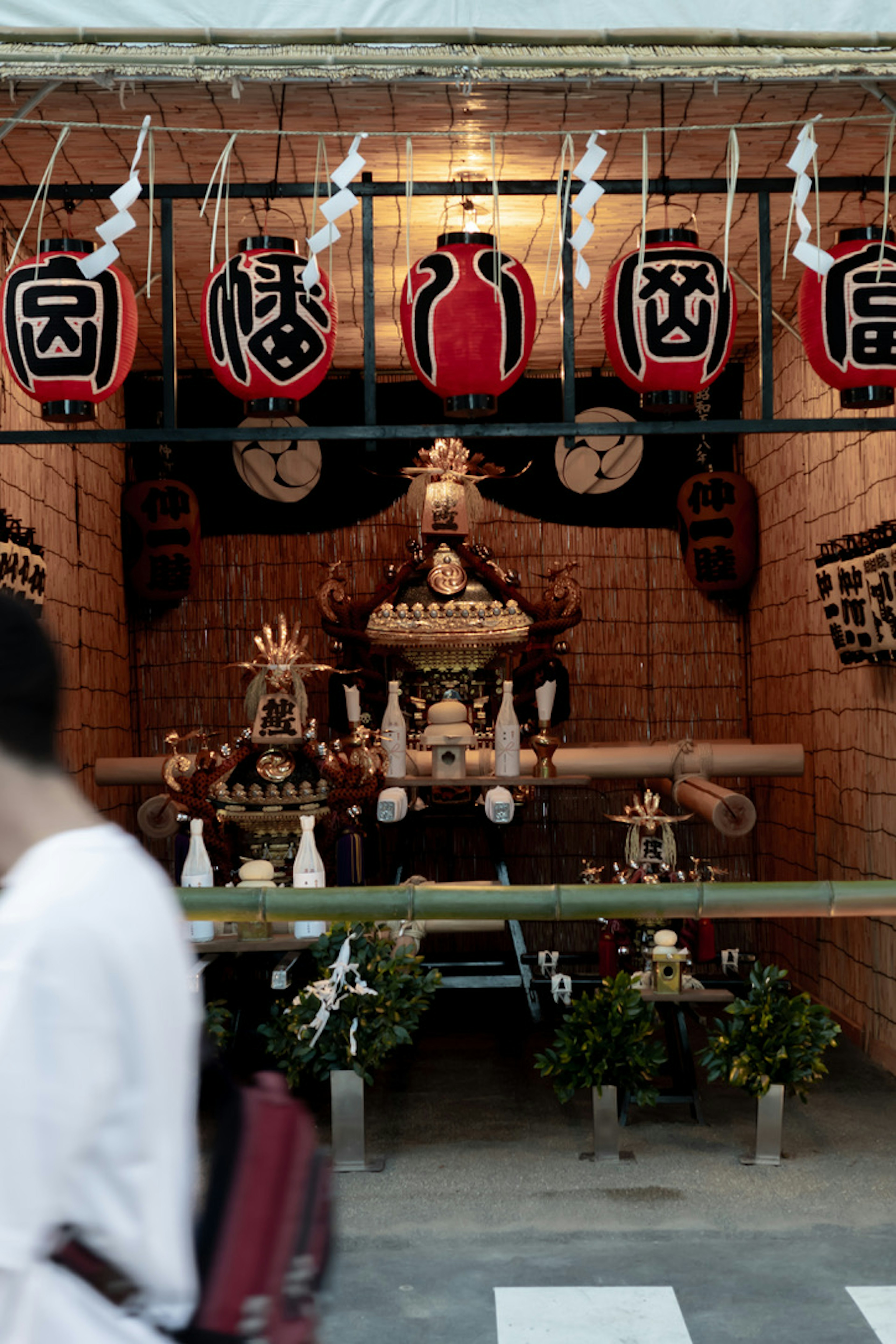 Un sanctuaire de festival décoré de lanternes et d'offrandes avec une personne passant