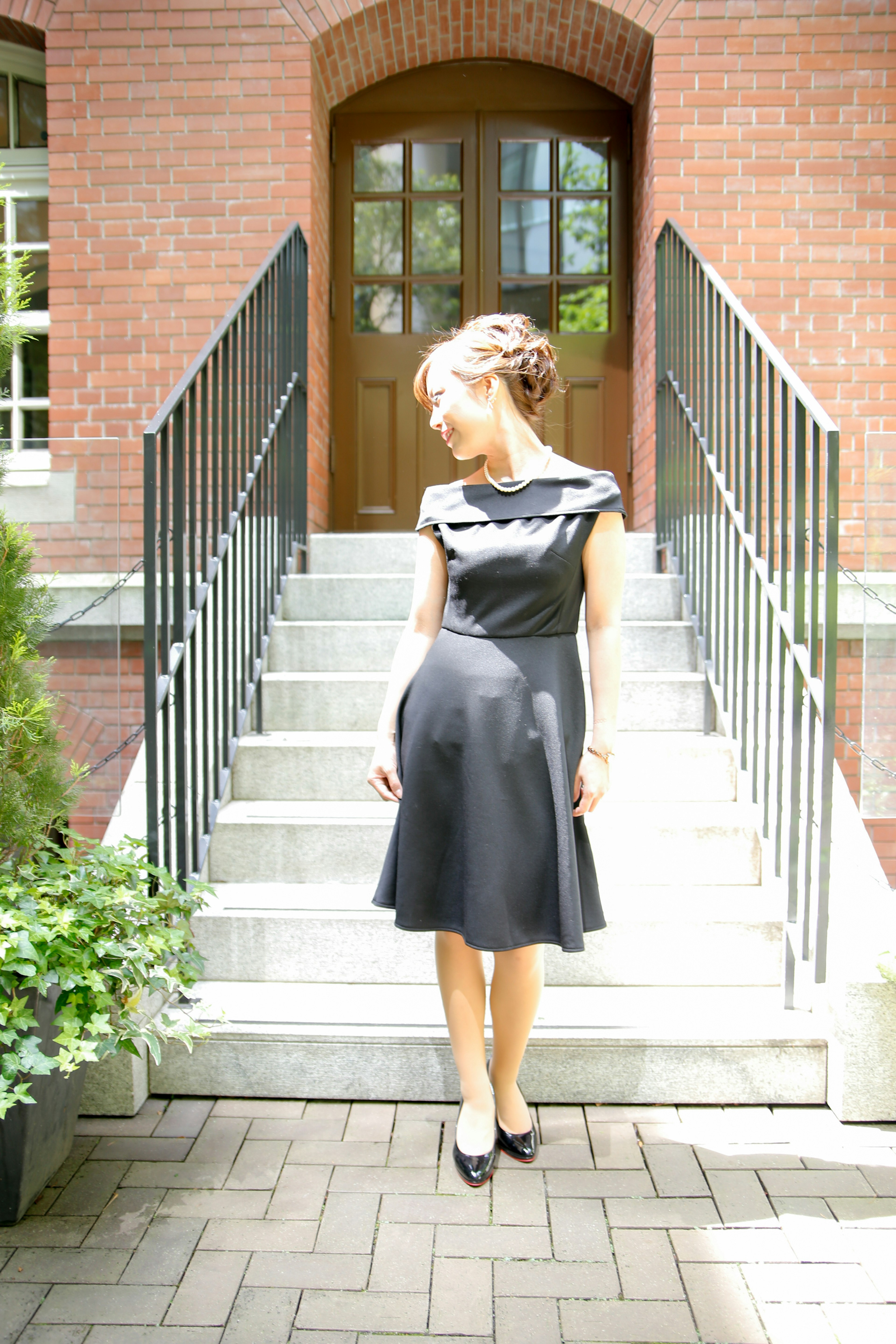 A woman in a black dress stands in front of stairs