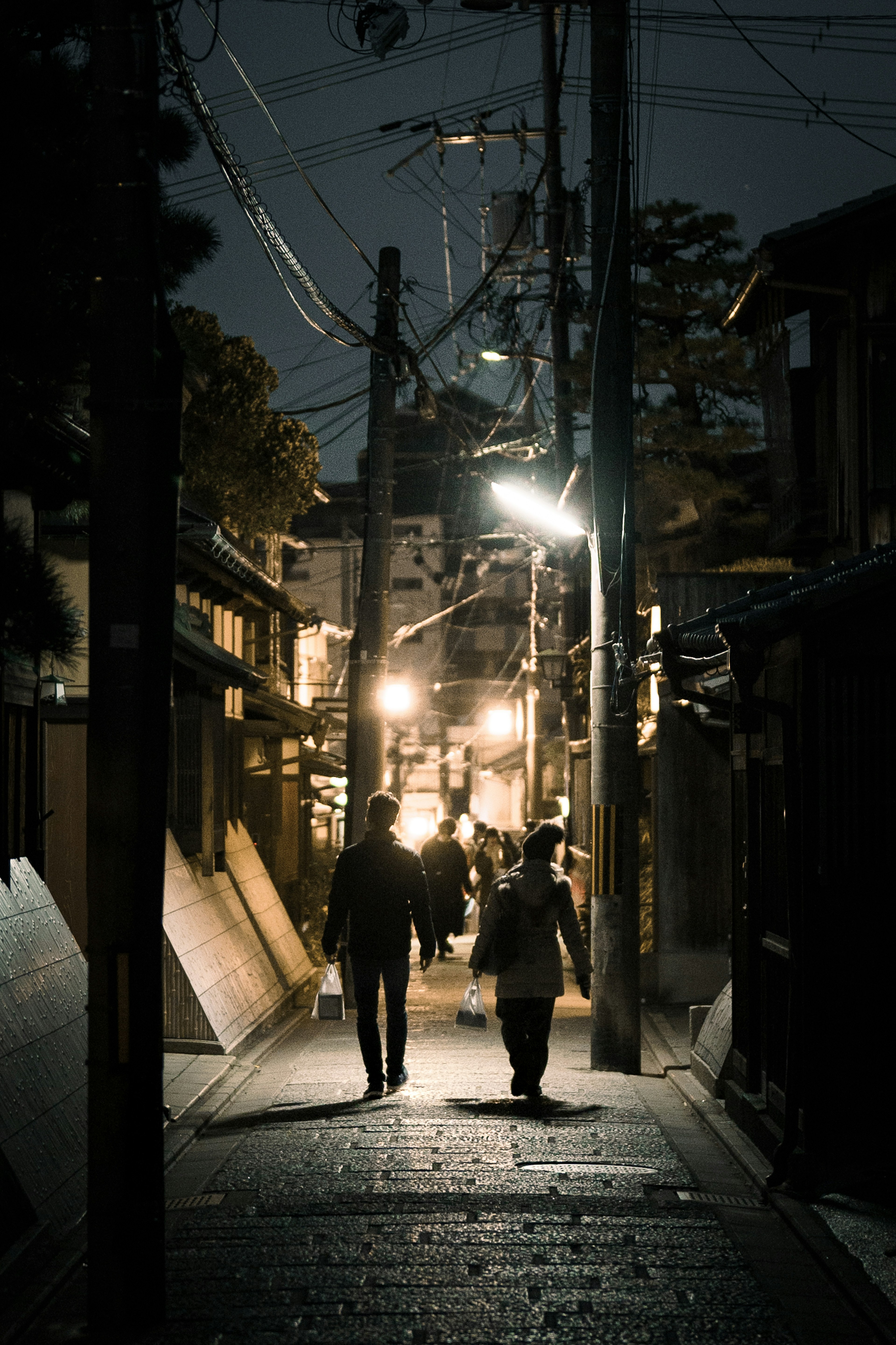 People walking in a narrow street at night illuminated by street lights