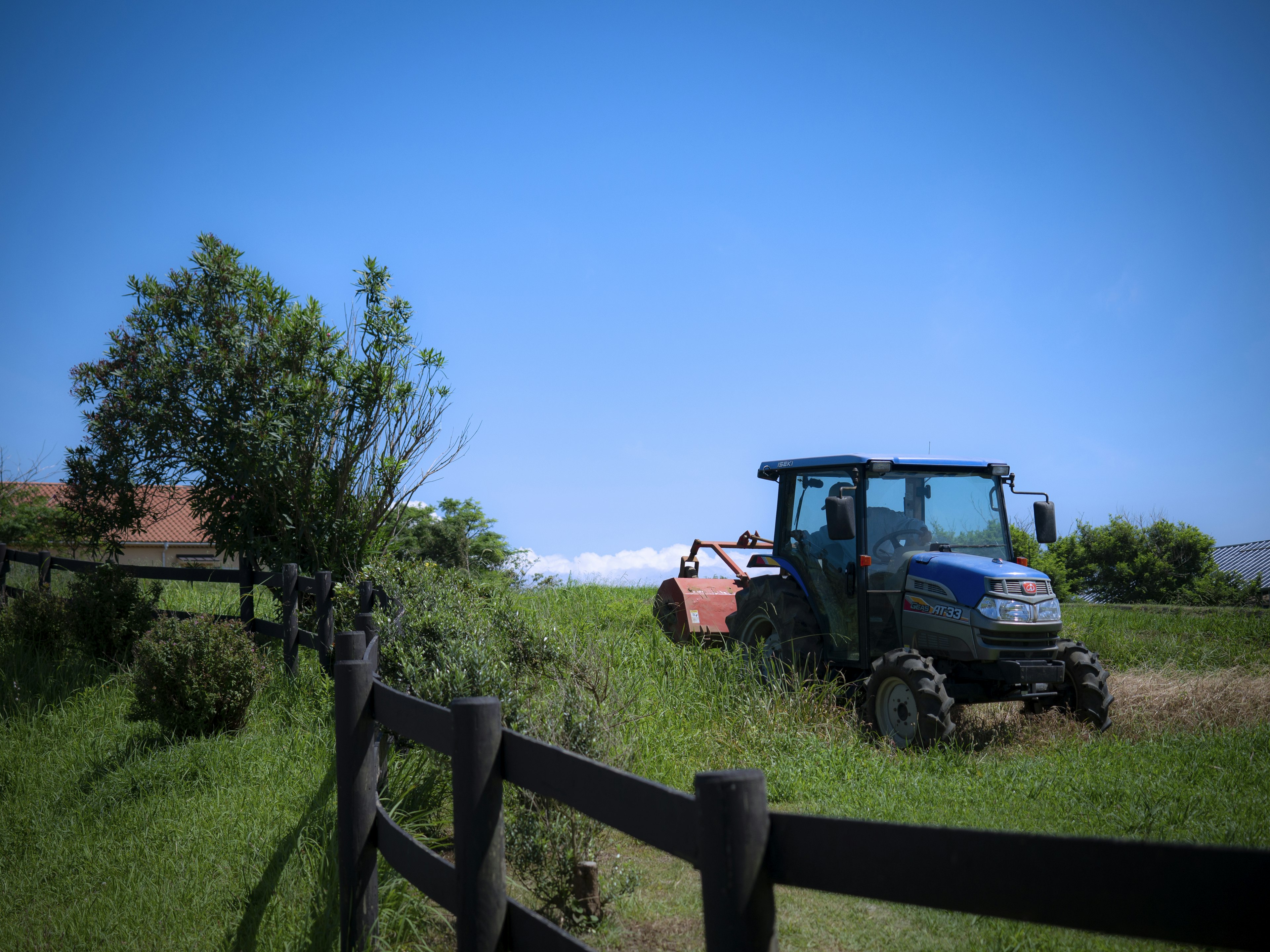 Tractor mowing grass under a blue sky with green landscape