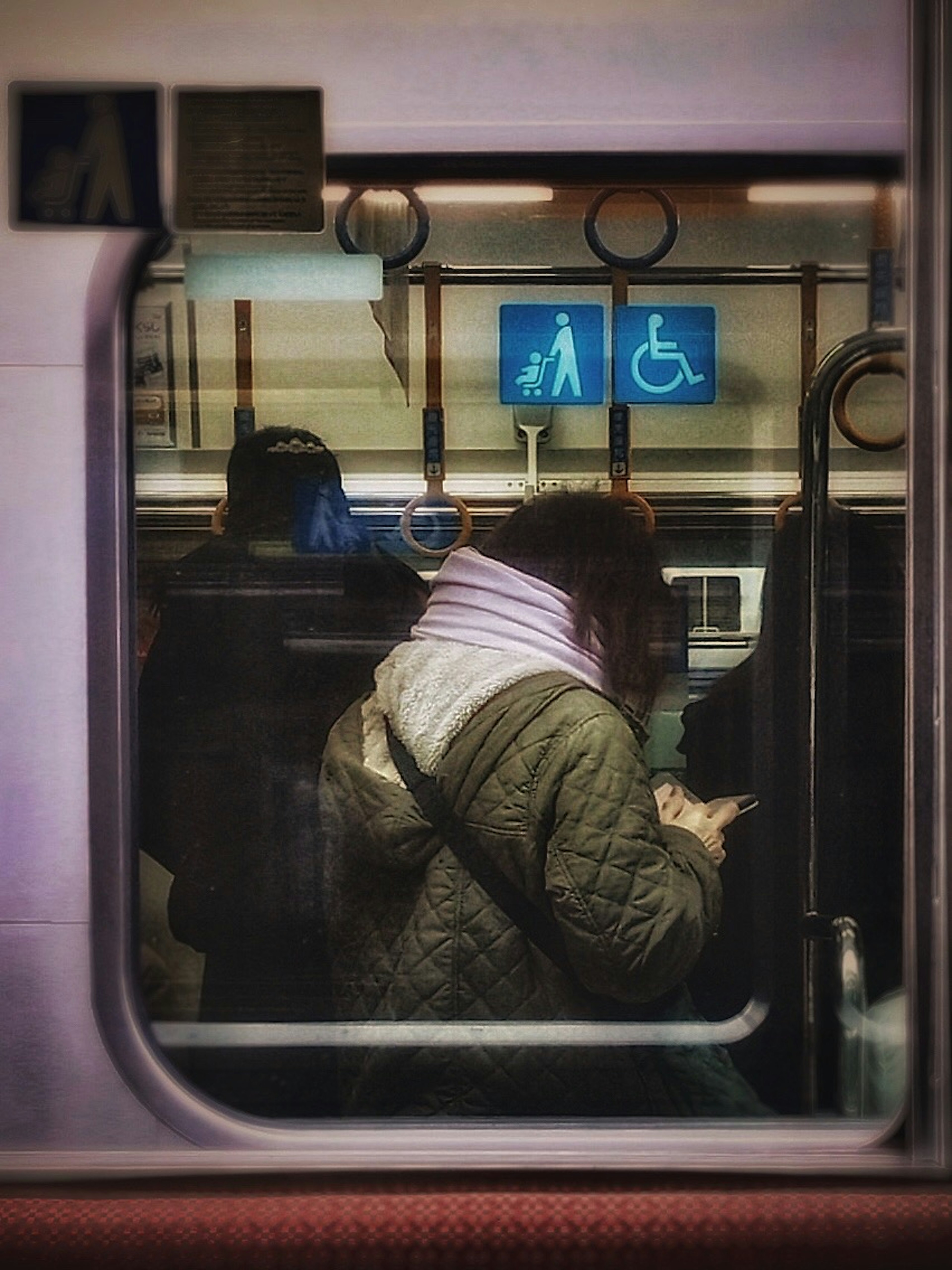 電車の中でスマートフォンを操作している女性の後ろ姿