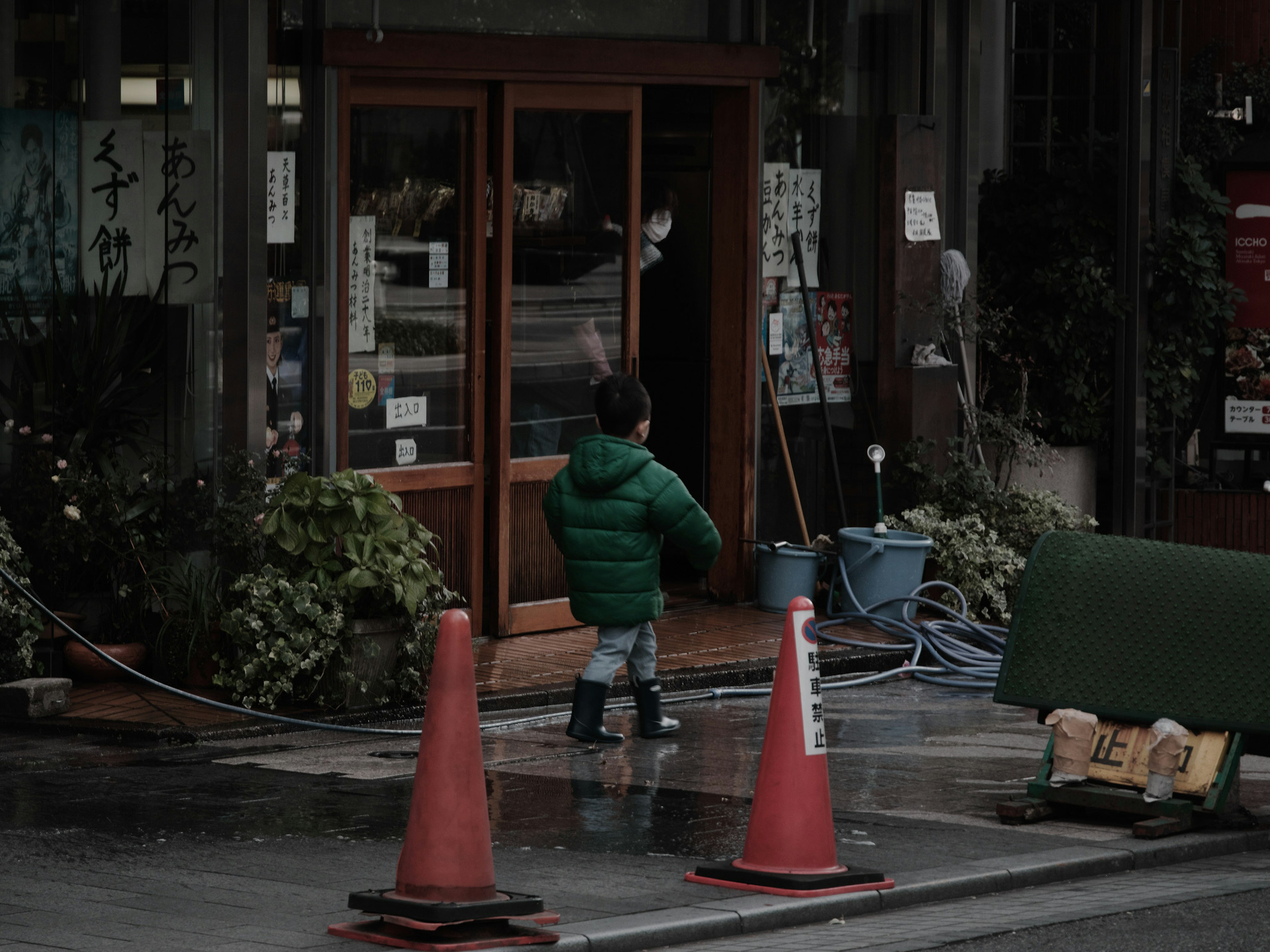 A child in a green jacket walking towards a shop entrance