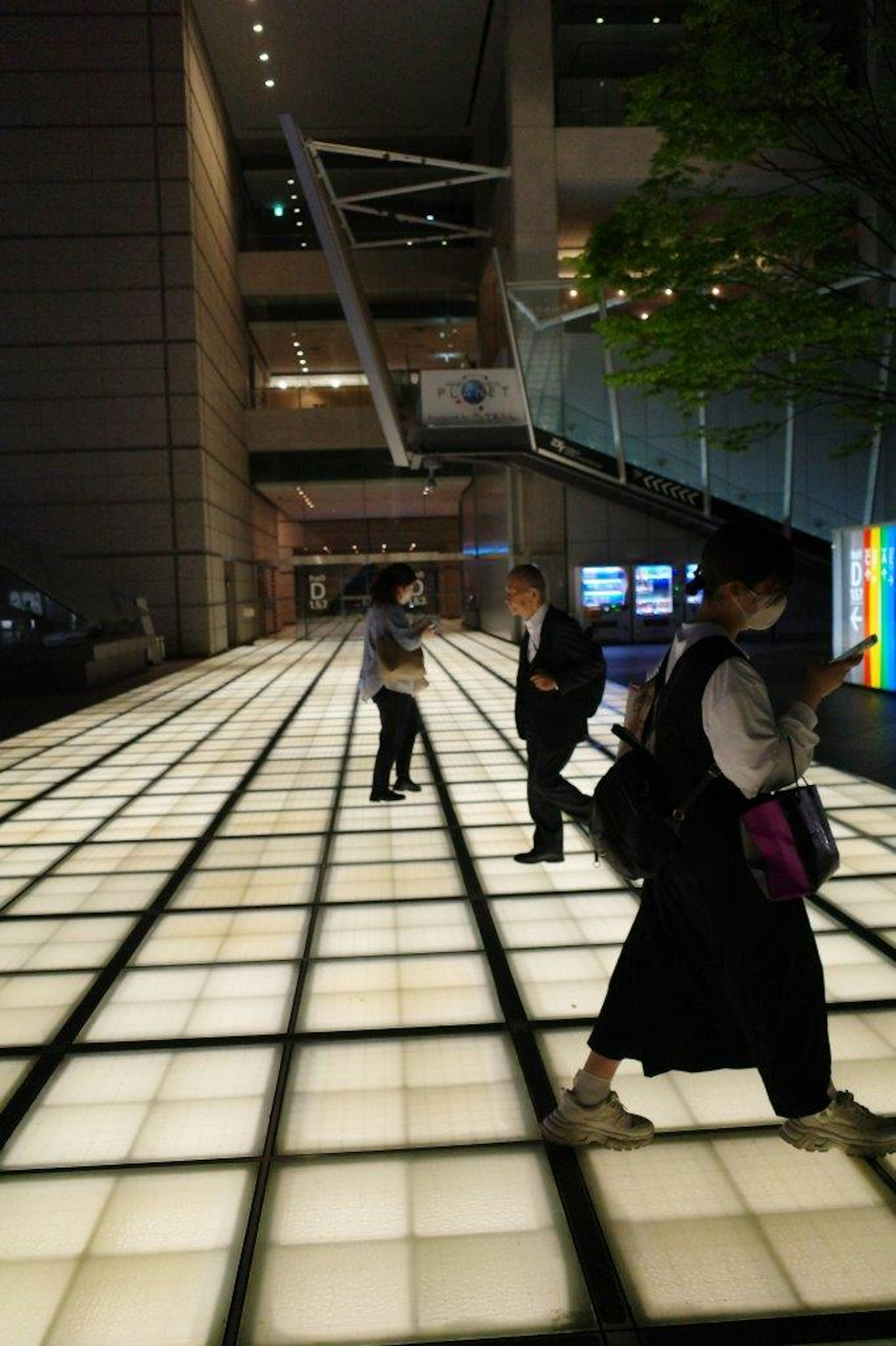 Paesaggio urbano notturno con persone che camminano su un pavimento luminoso