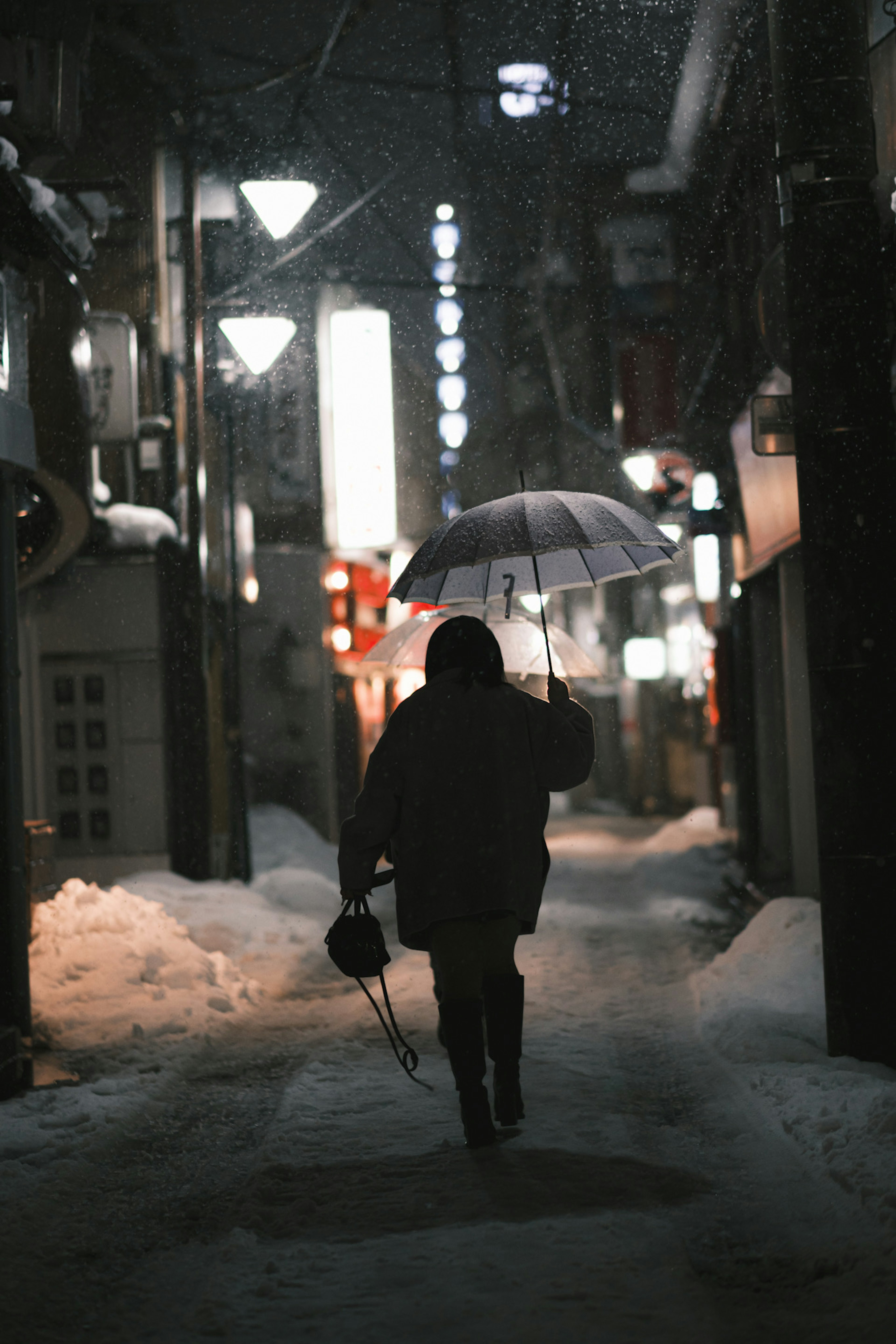 Silhouette of a person walking with an umbrella in the snow at night