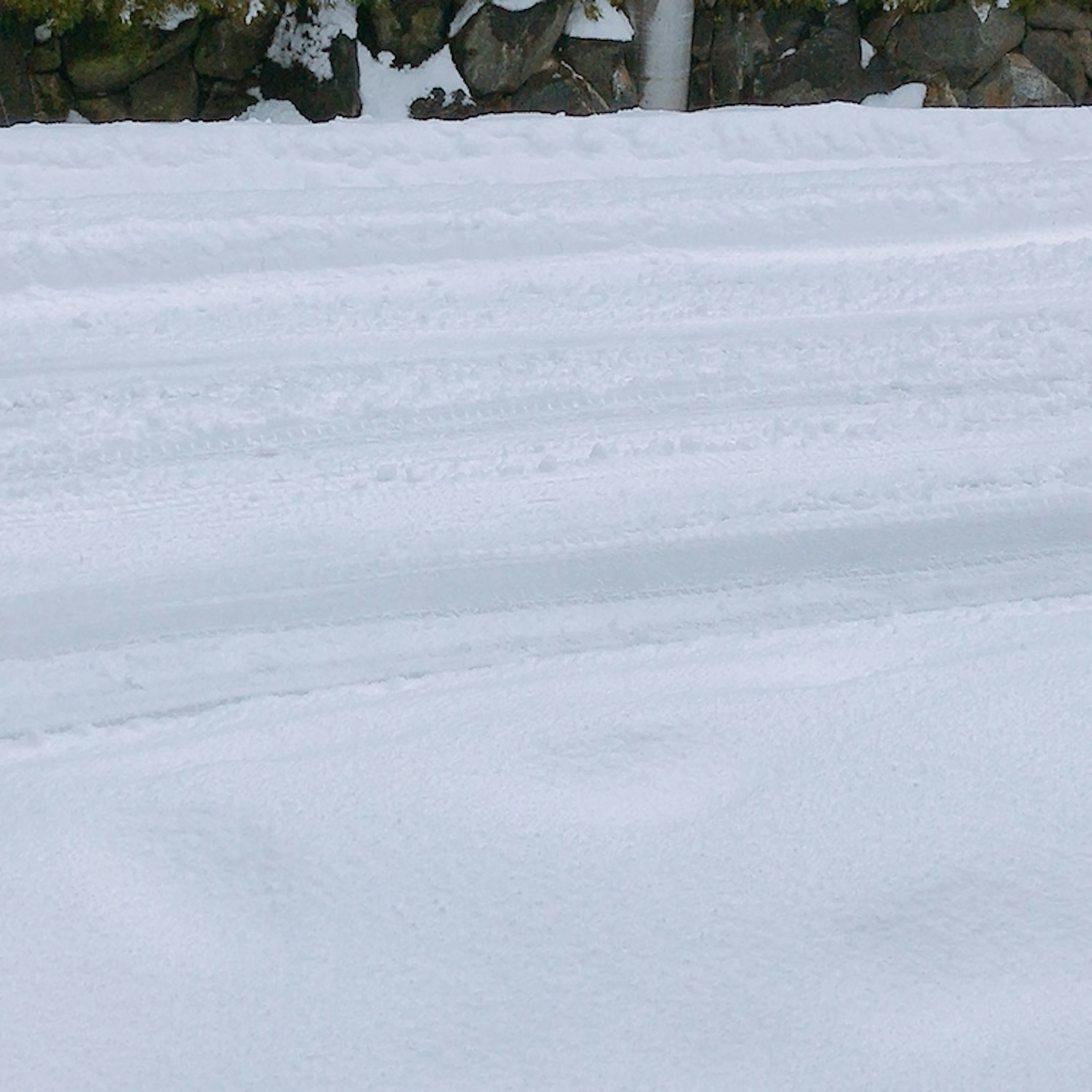 Snow-covered road with tire tracks and stone wall