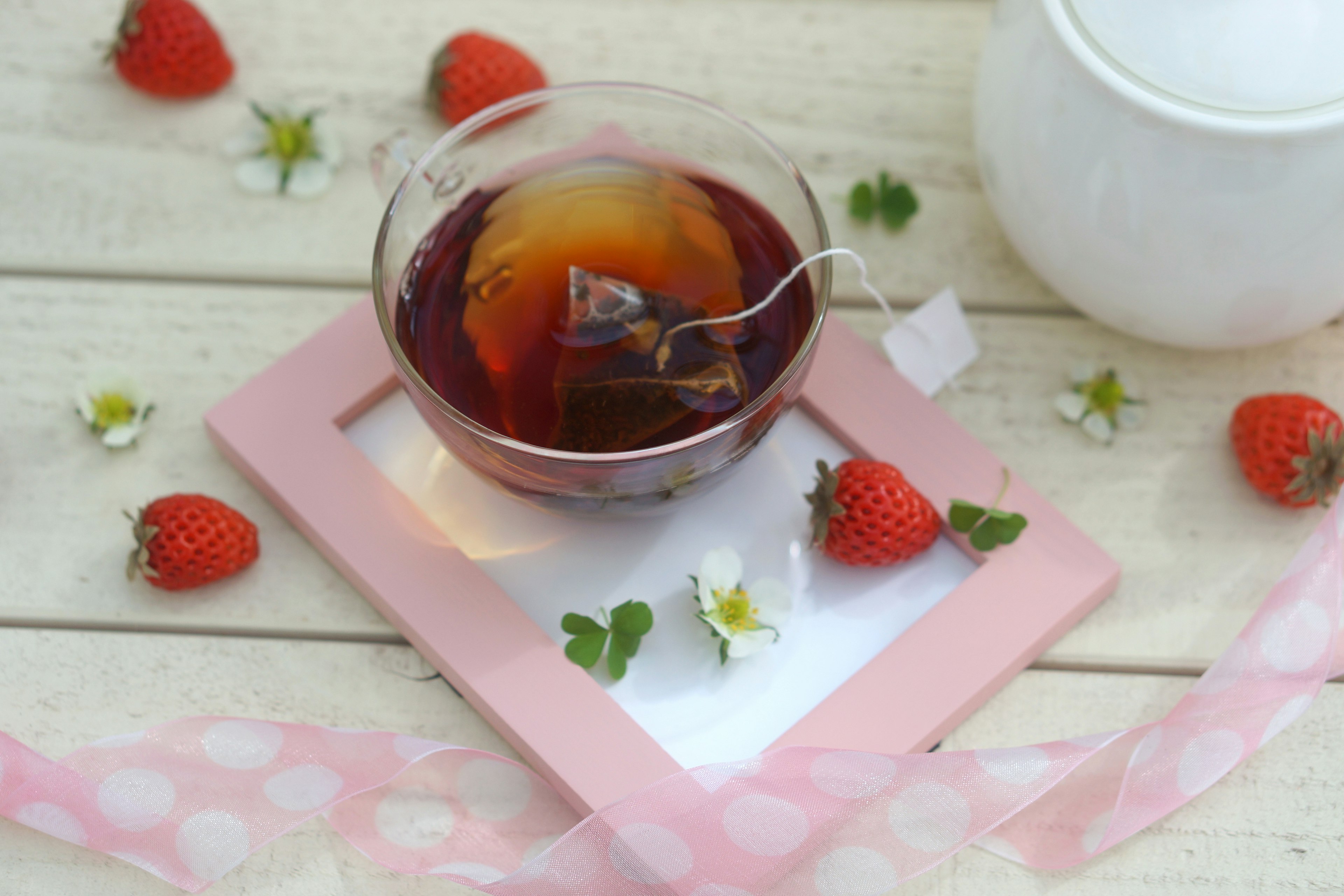 Taza transparente con bolsa de té y fresas dispuestas sobre una mesa