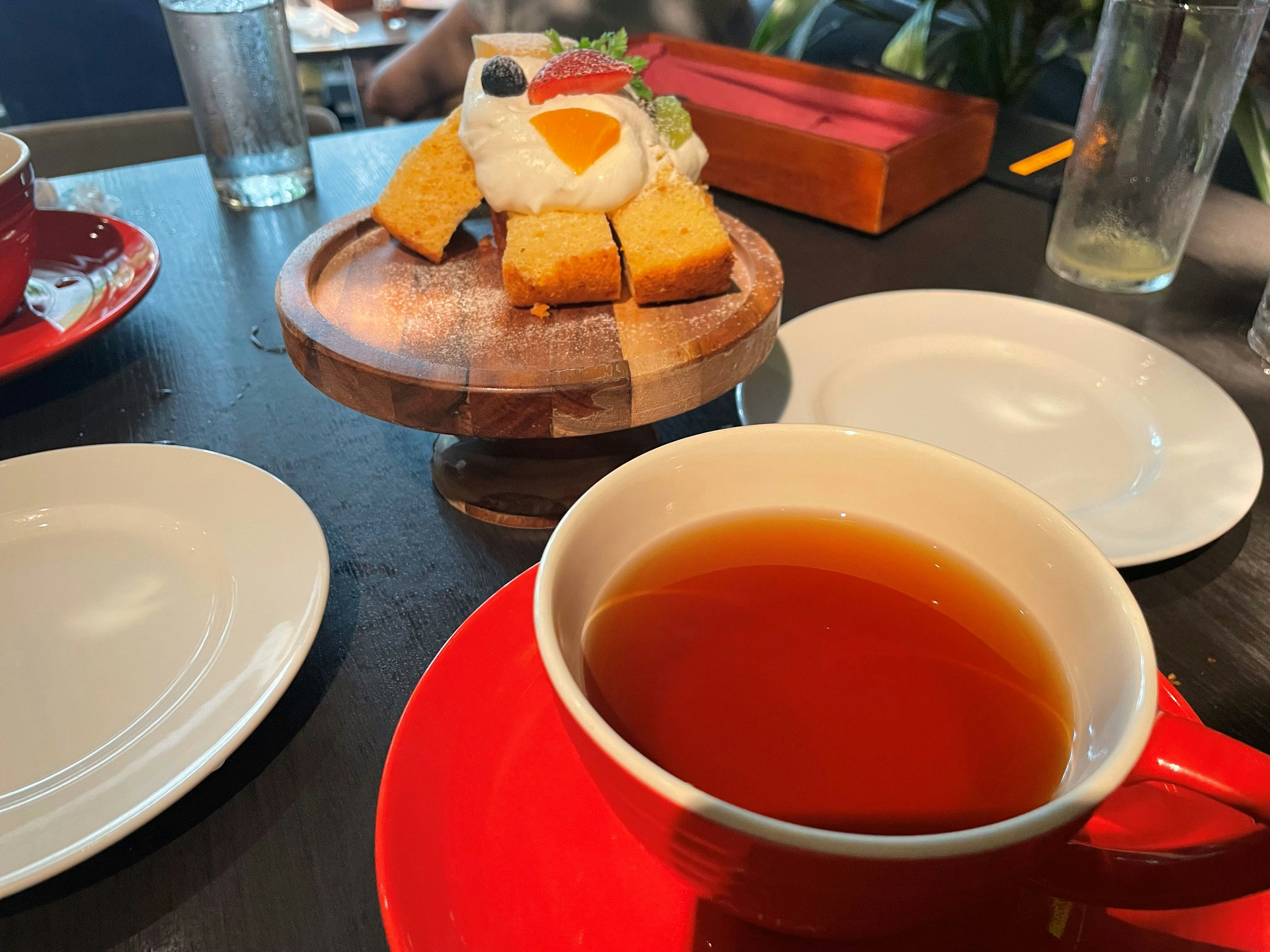 Rote Tasse Tee mit Tellern um einen Holzständer mit einem dekorativen Dessert