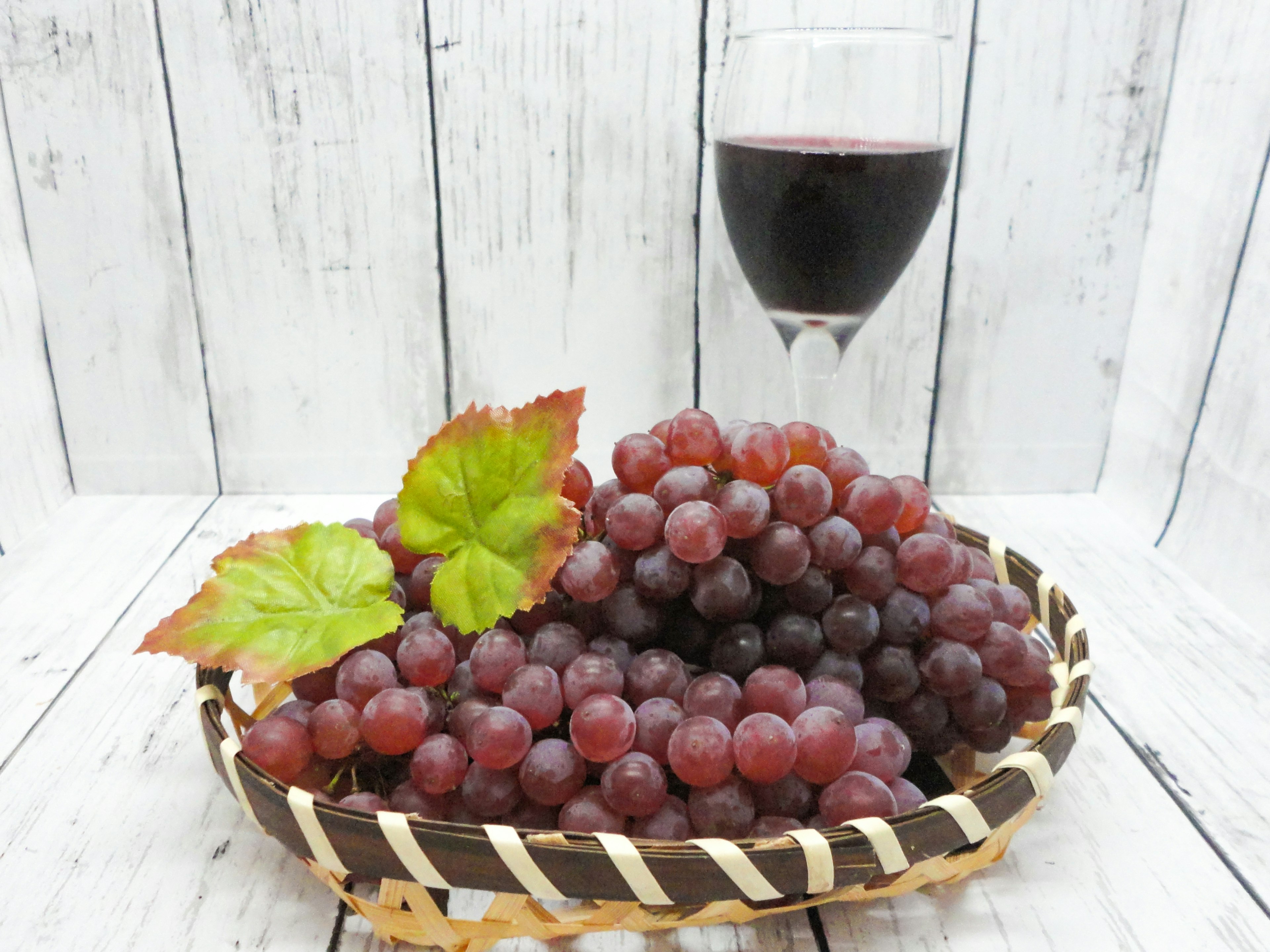 A bunch of red grapes in a woven basket with a glass of red wine in the background