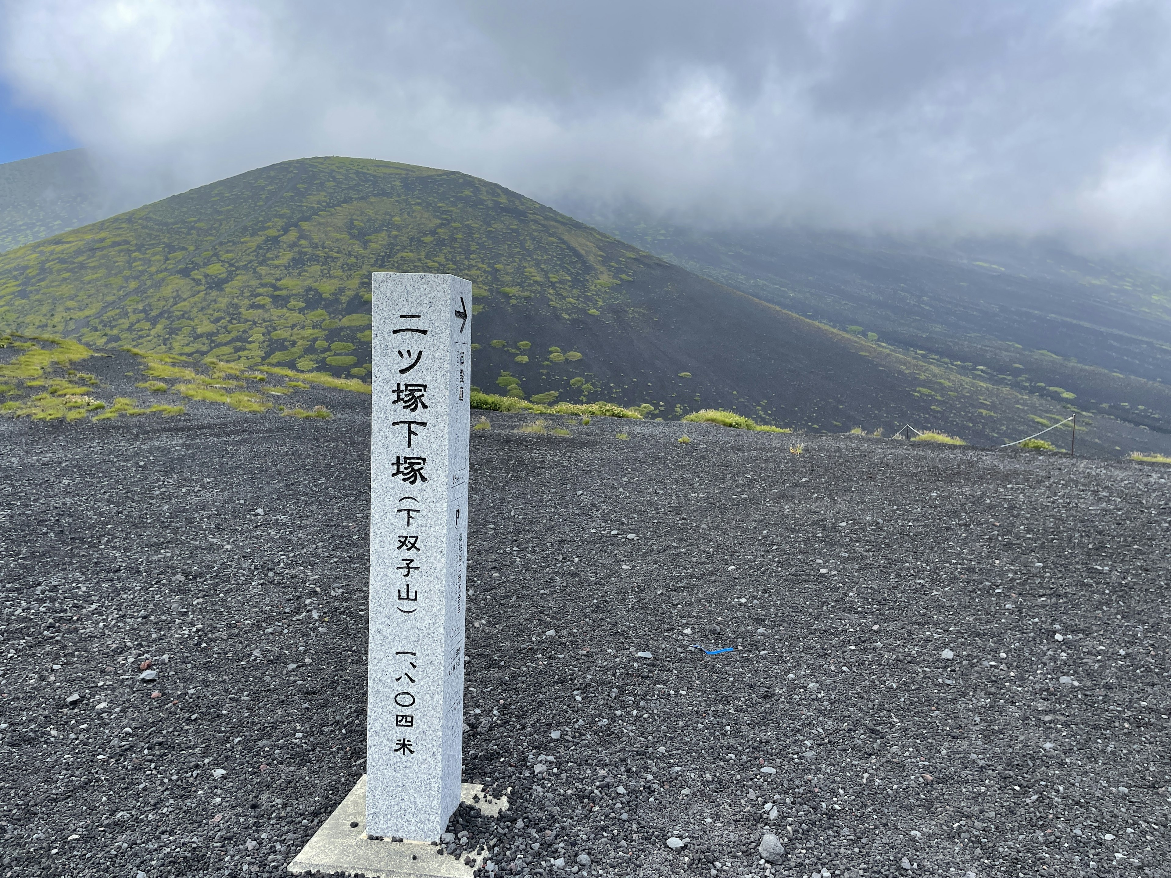 Cartello sul sentiero del Monte Fuji con una montagna verde sullo sfondo