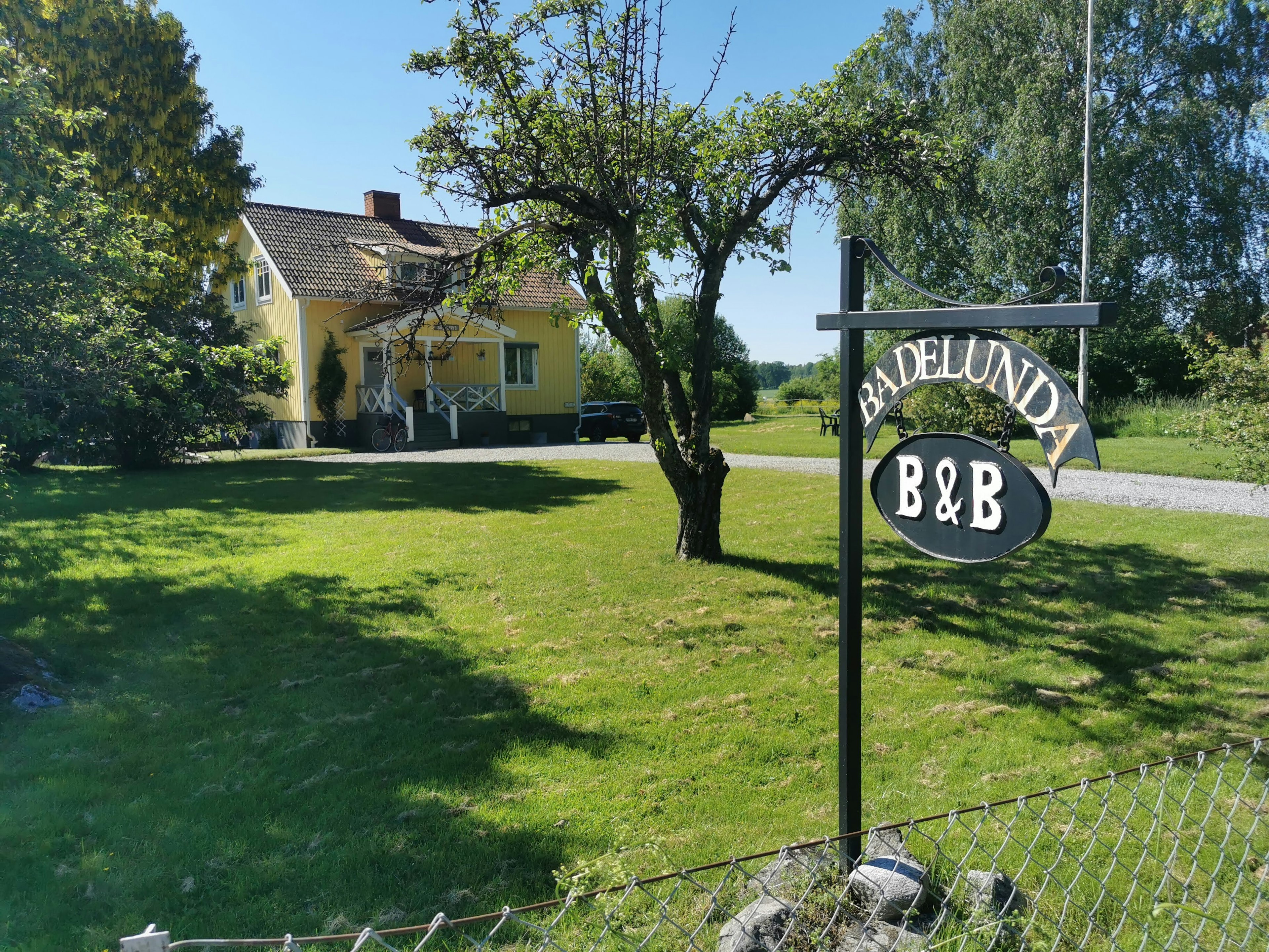 Badelunda B&B sign with a charming yellow house and green lawn