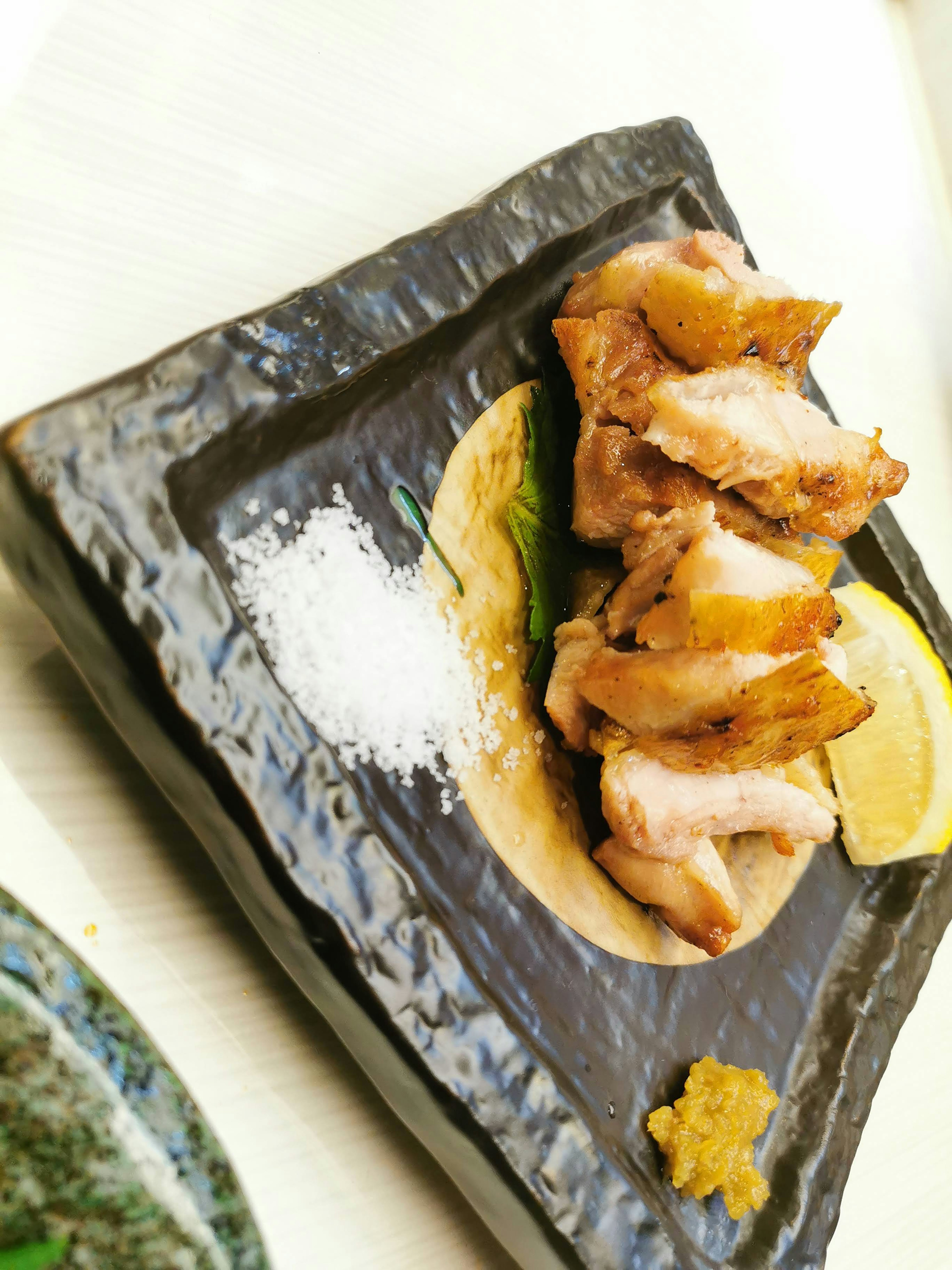 Grilled chicken presented on a black plate with lemon and salt garnishes