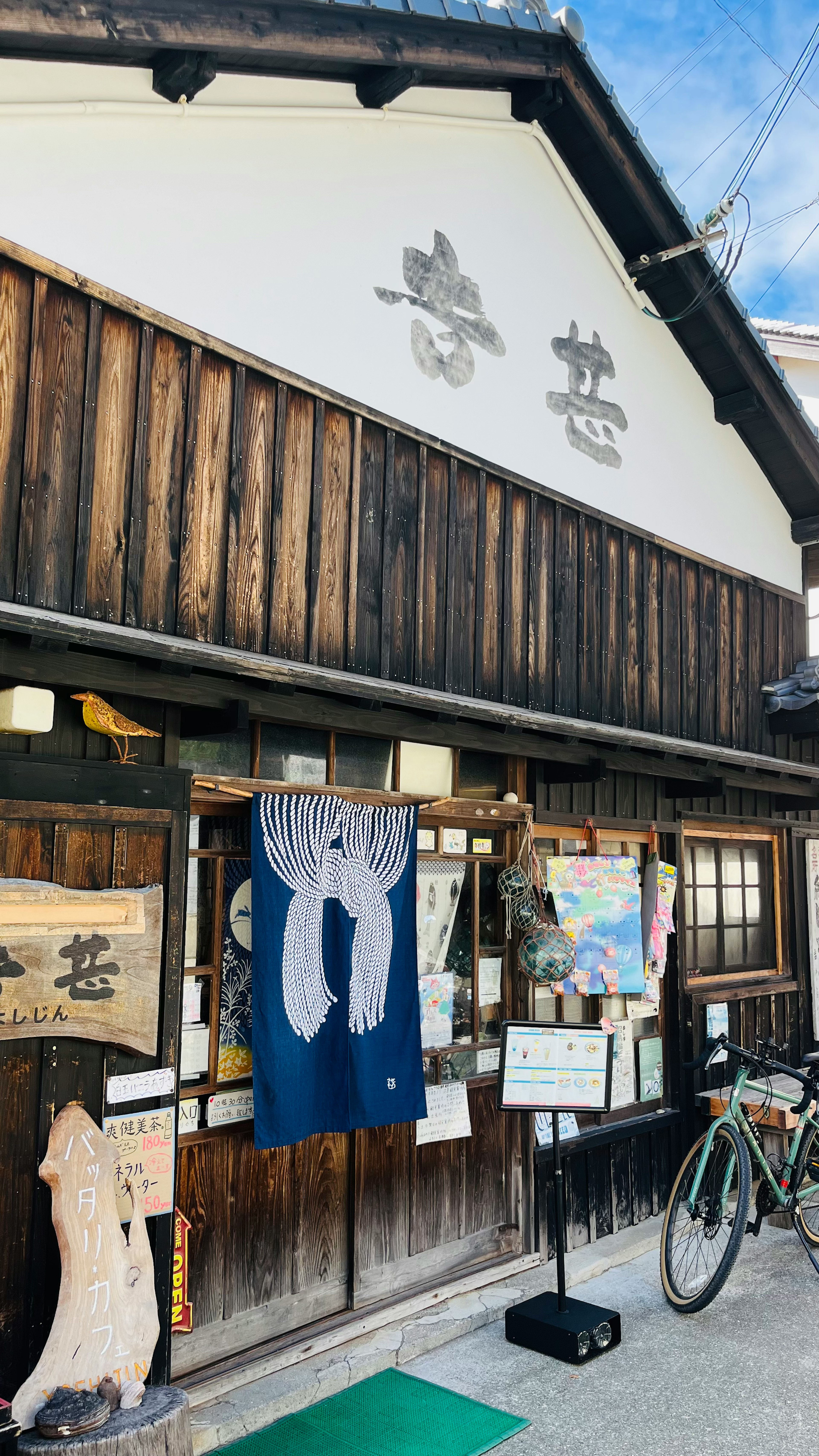 Eksterior toko Jepang tradisional dengan dinding kayu dan papan kanji dengan noren biru tergantung