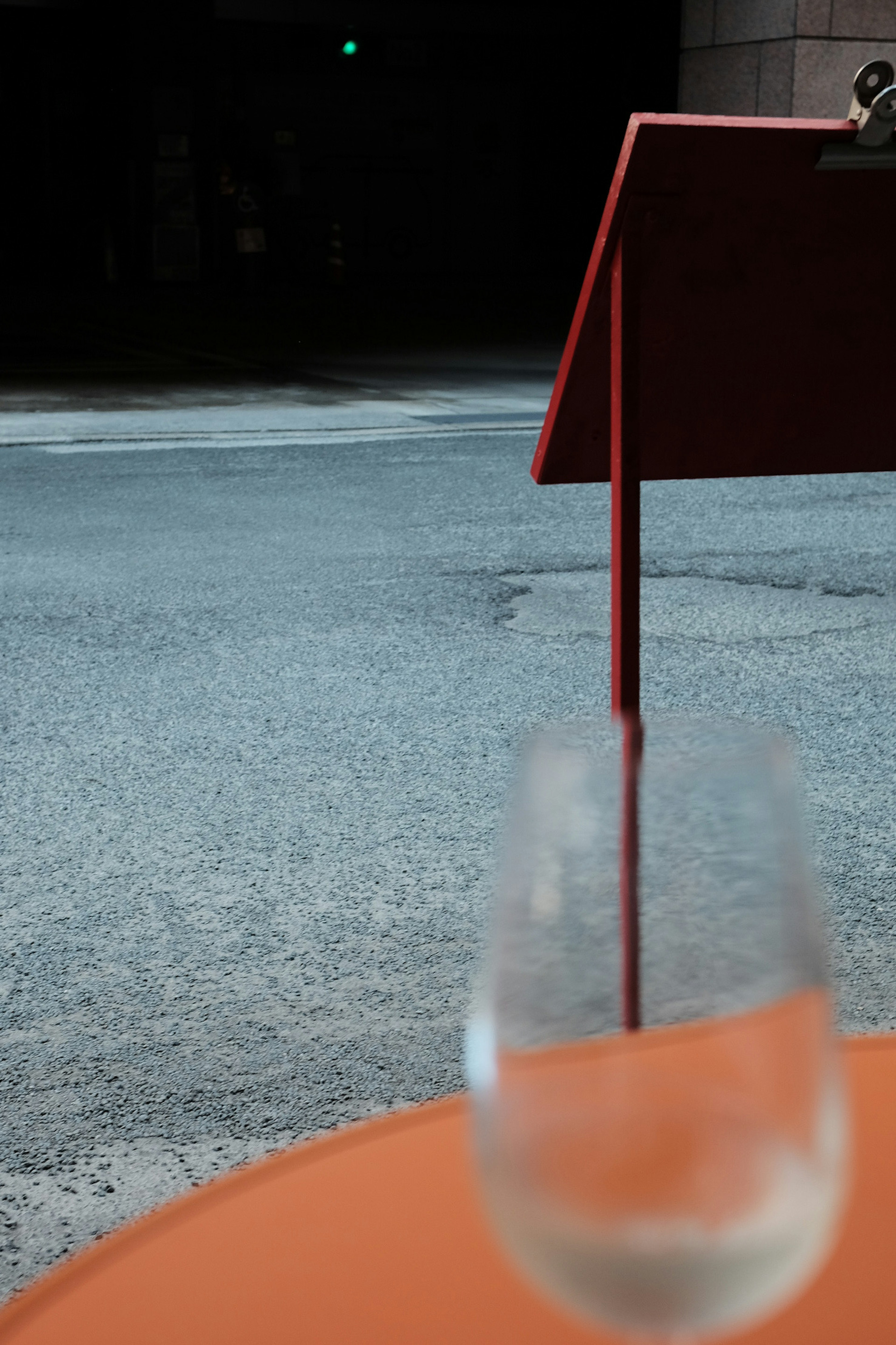 Un vaso transparente sobre una mesa naranja con un soporte rojo al fondo